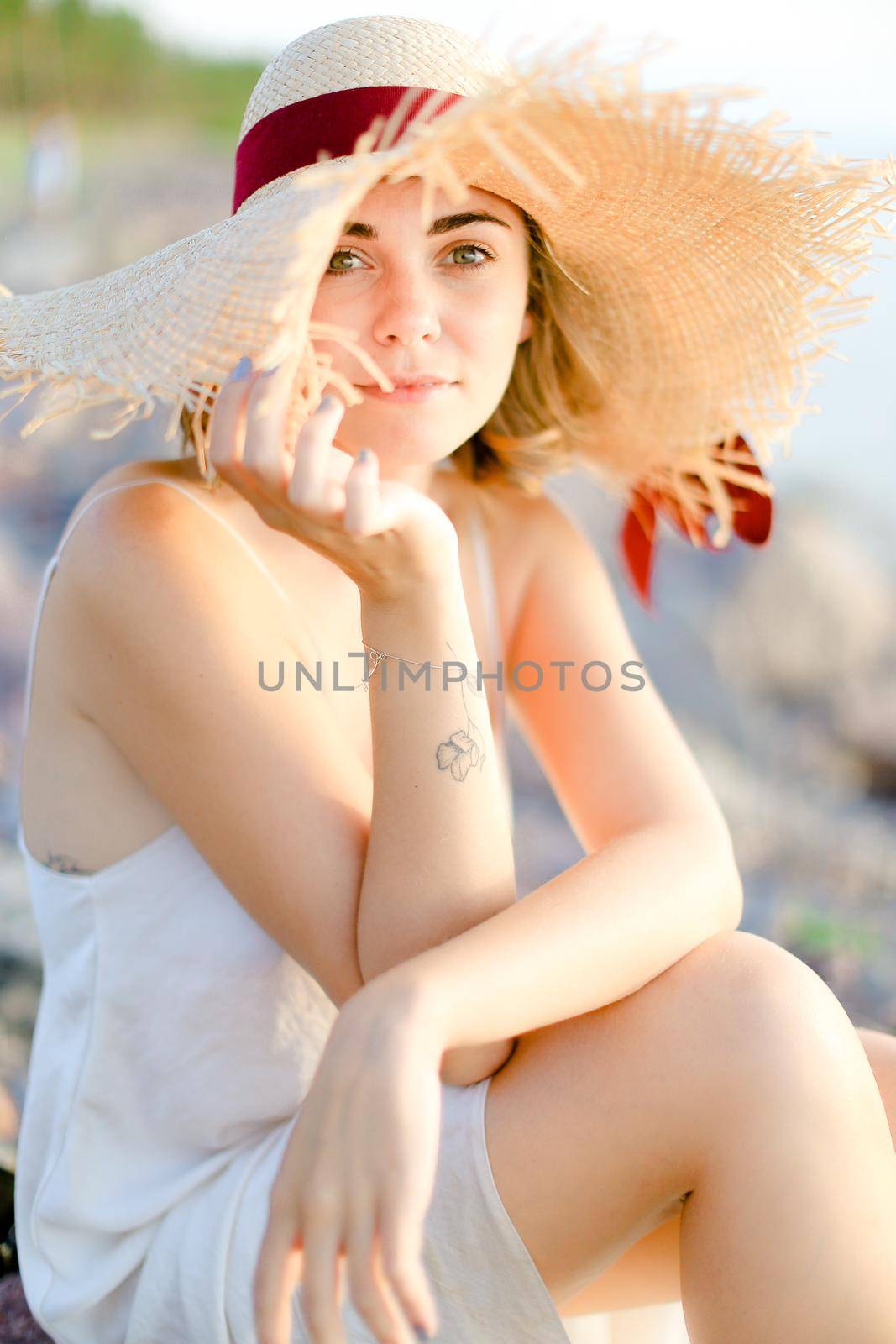 Back view of woman in hat with red ribbon walking on shingle beach. Concept of summer vacations and resort.