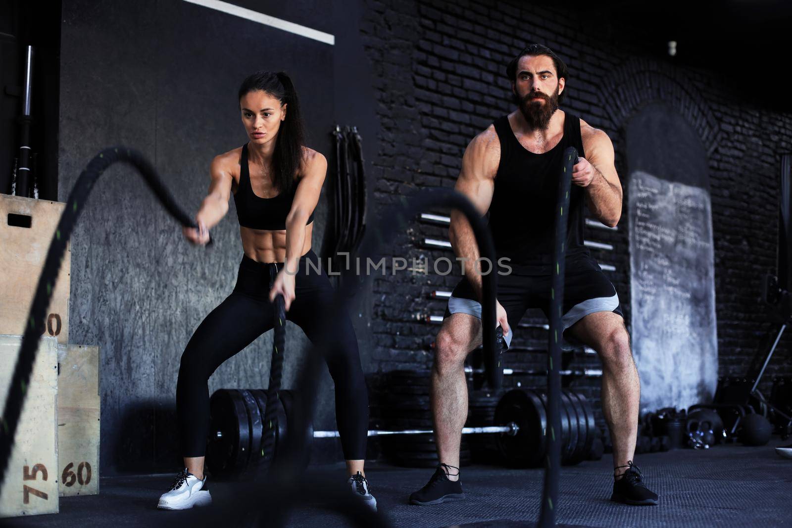 Athletic young couple with battle rope doing exercise in functional training fitness gym. by tsyhun