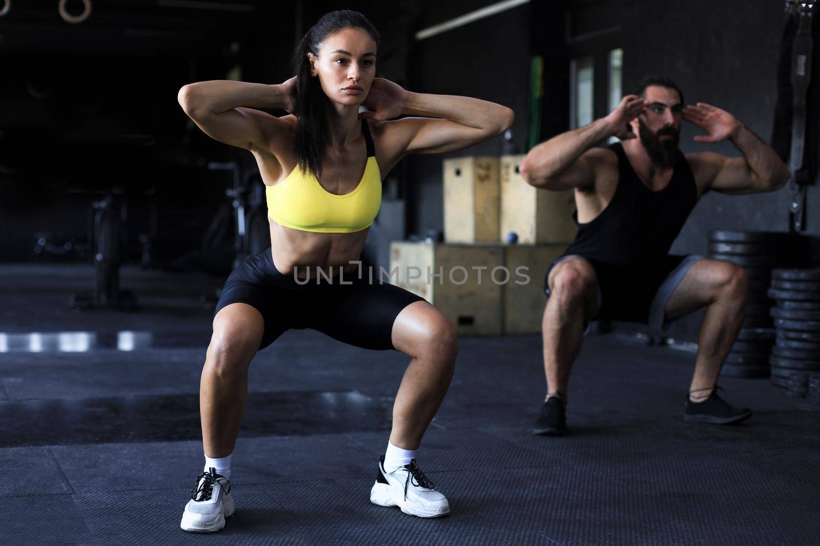 Fitness couple in sportswear doing squat exercises at gym