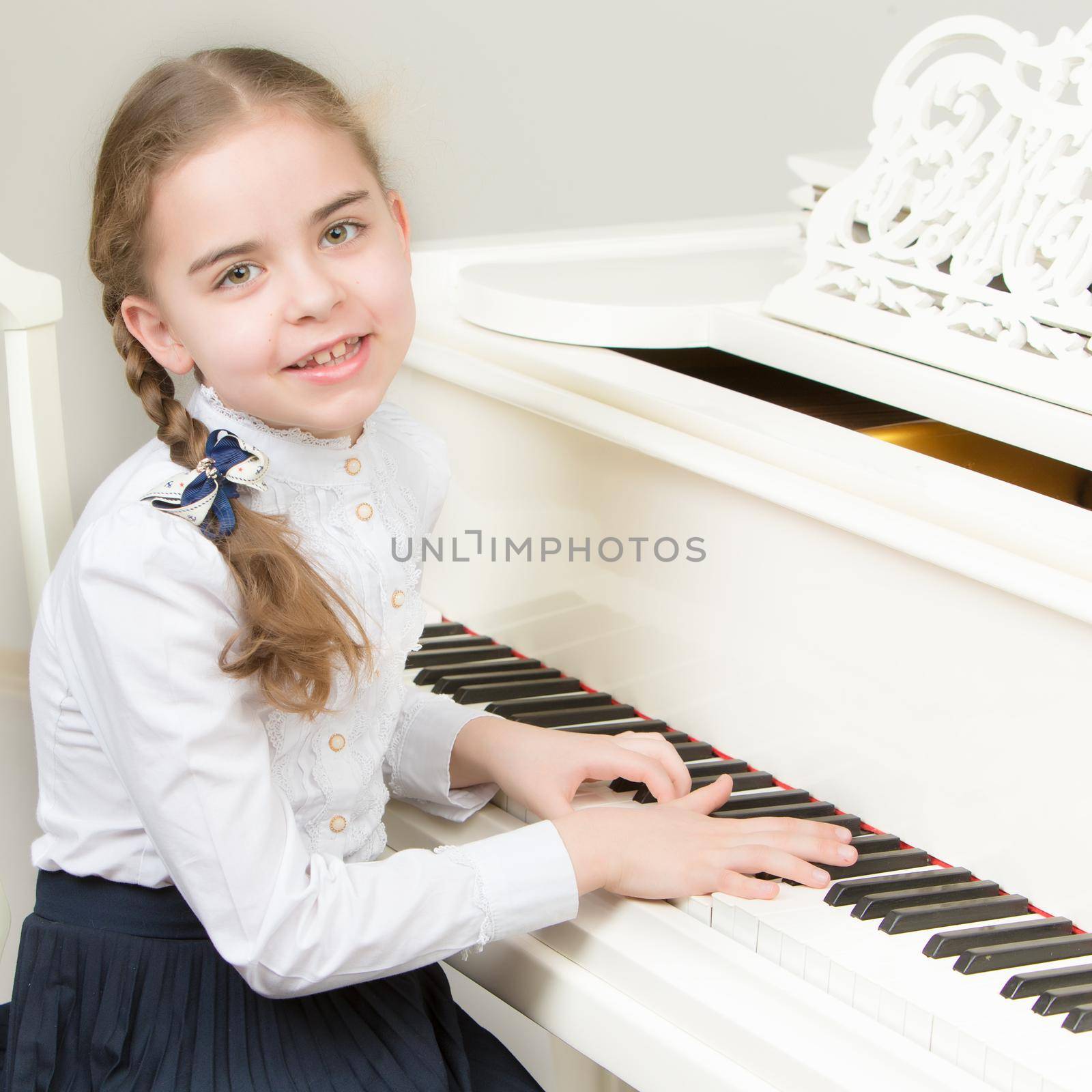 Charming little blonde with long wattled hair in plaits, playing on a white grand piano. In musical school.