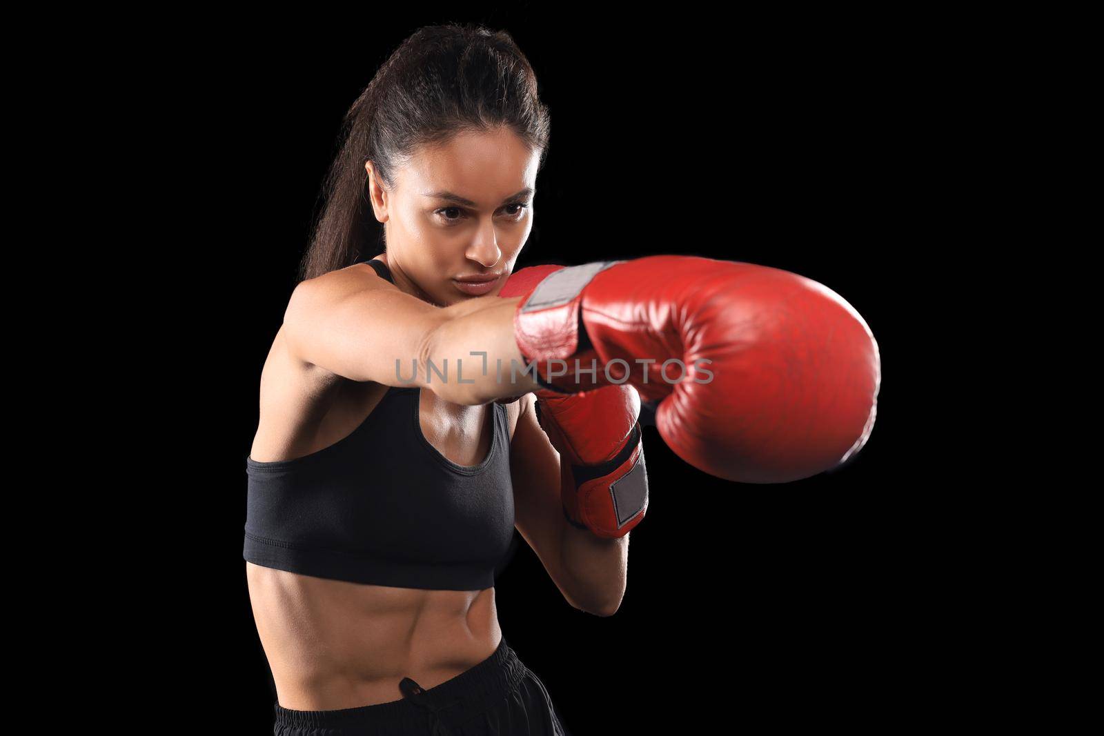 Kickboxing woman in activewear and red kickboxing gloves on black background performing a martial arts kick. Sport exercise, fitness workout