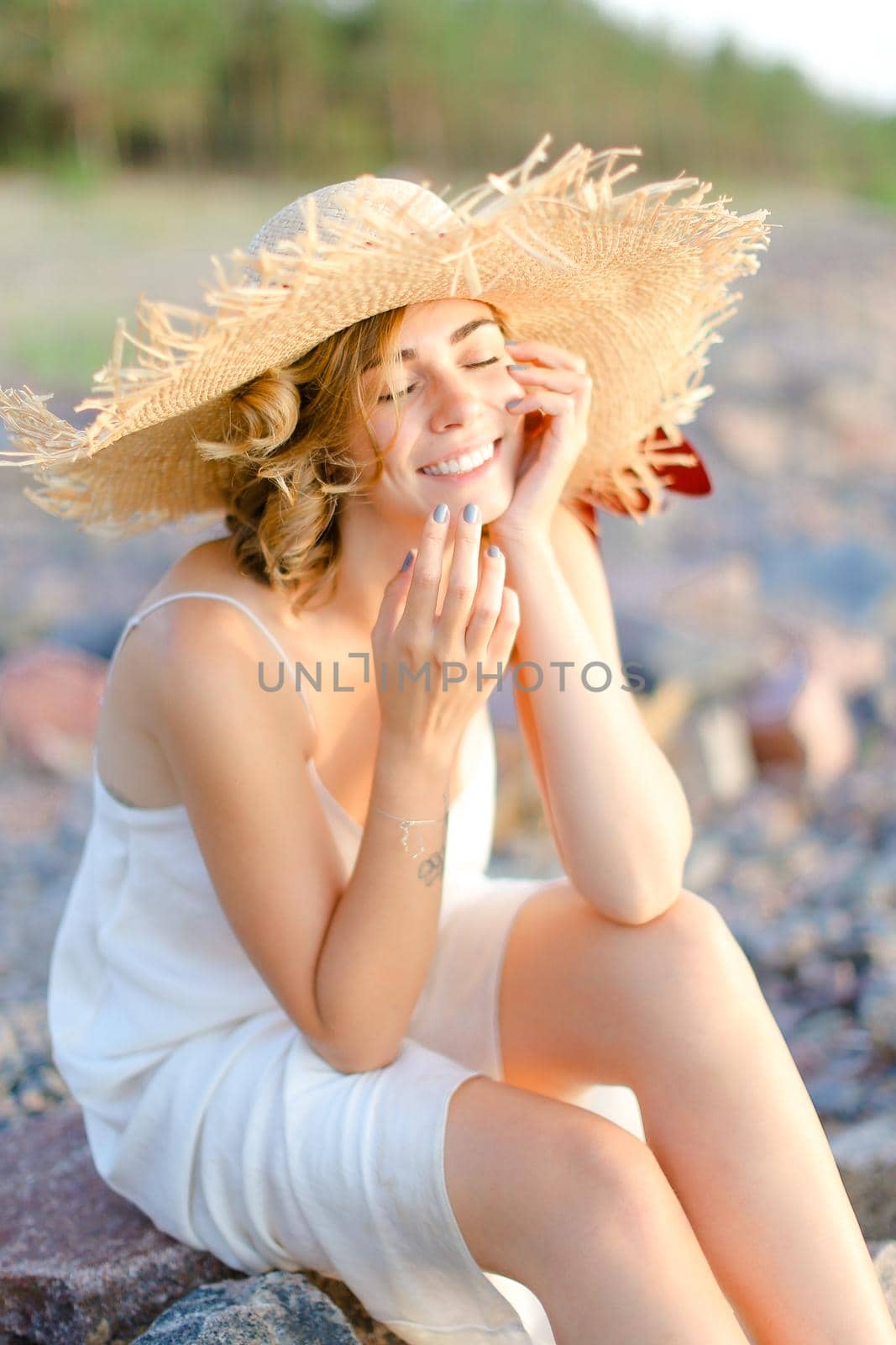 Young charming woman in hat sitting on shingle beach. by sisterspro