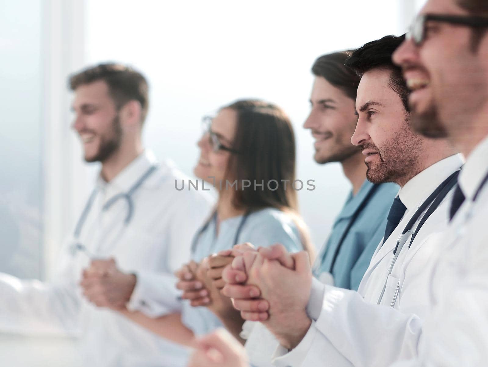 Happy group of people in white coats holding hands during a conference call.