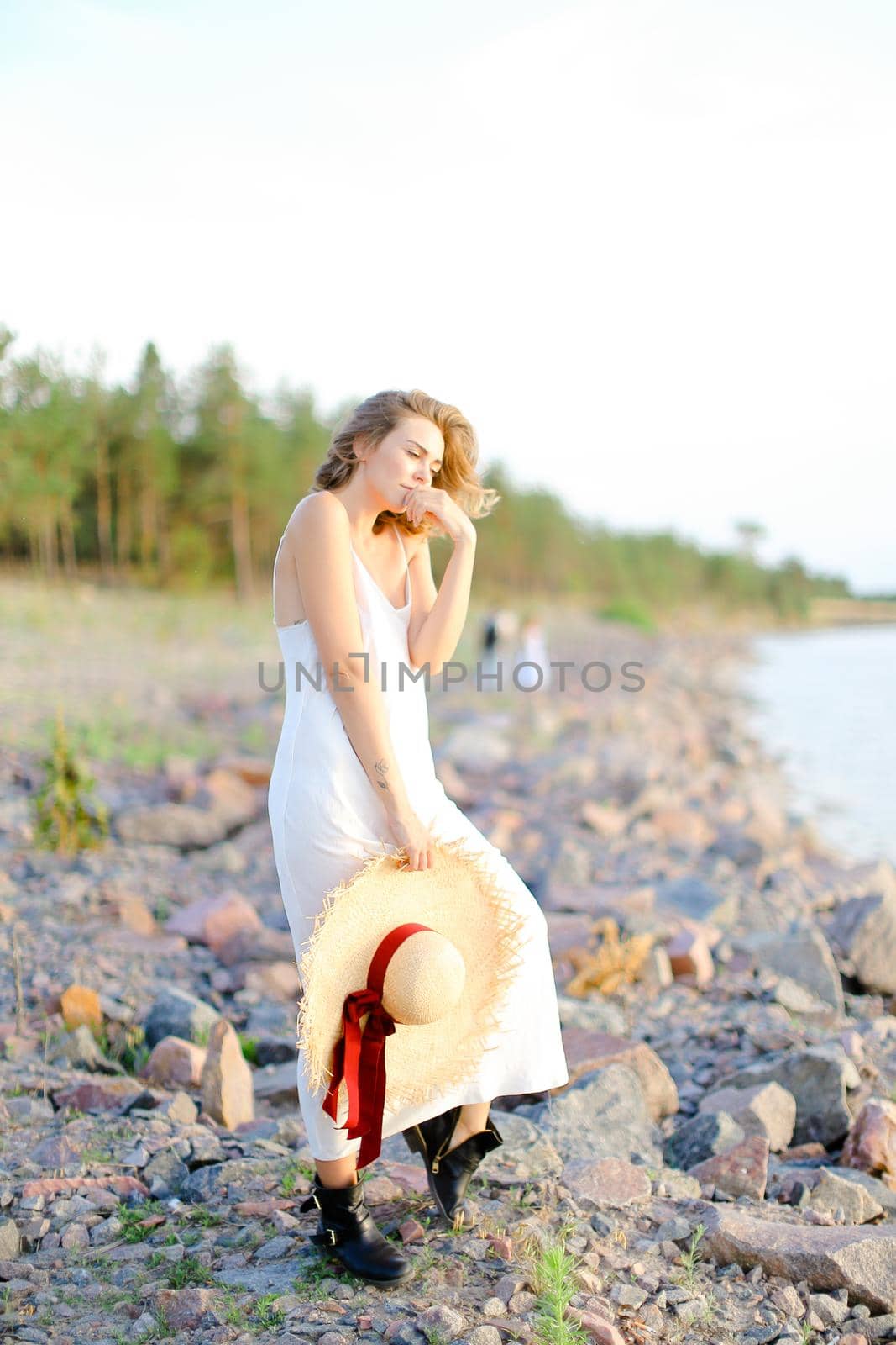 Caucasian pretty girl walking on shingle beach with hant in hands and wearing dress. Concept of summer vacations and fashion.