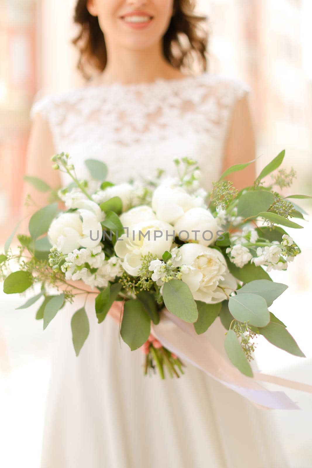 Happy smiling fiancee keeping bouquet of flowers and wearing white dress. Concept of bridal photo session and wedding.