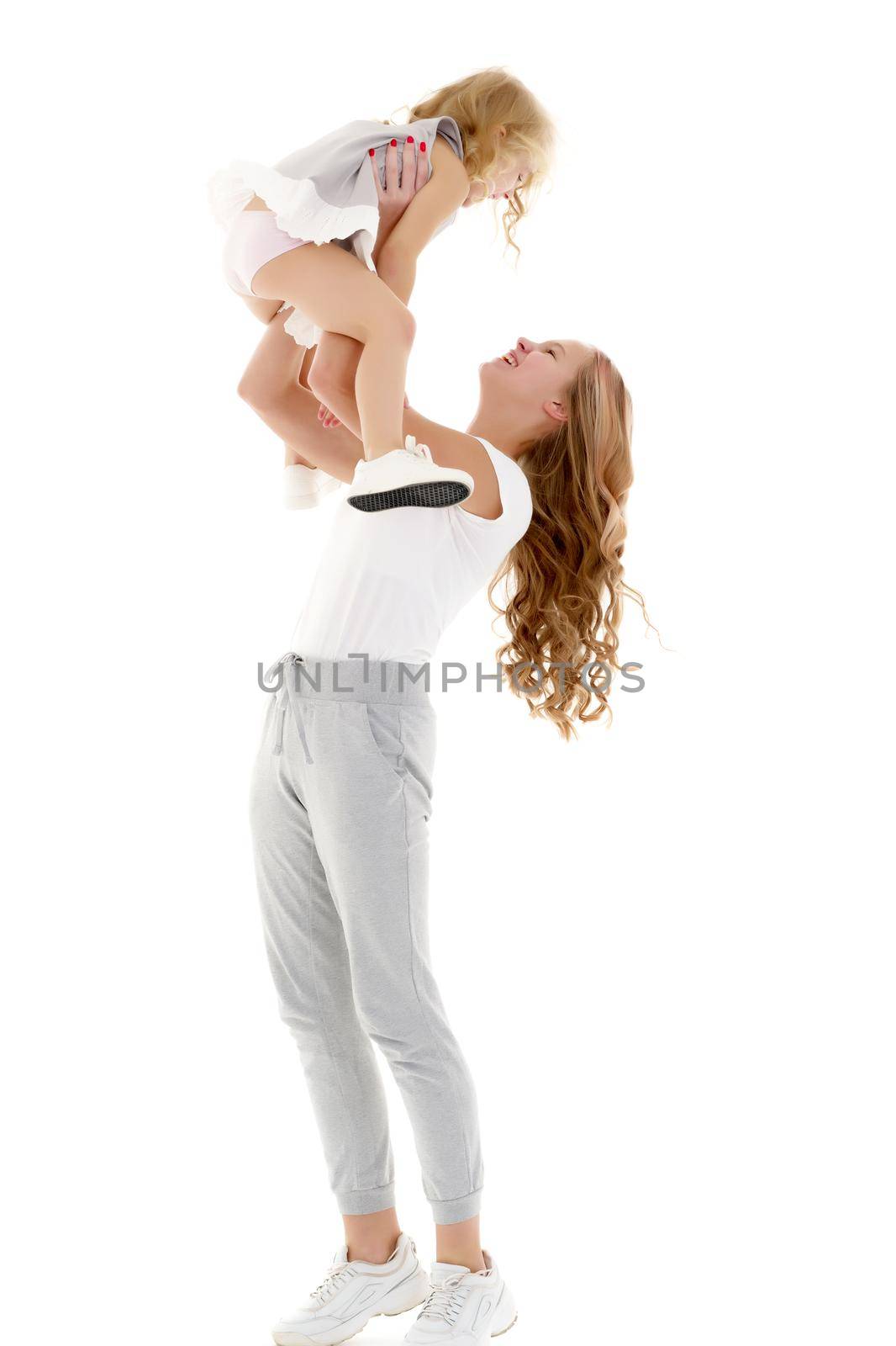 Beautiful young girl holding her little sister in her arms and looking at her with love. The concept of family happiness. Isolated on white background.