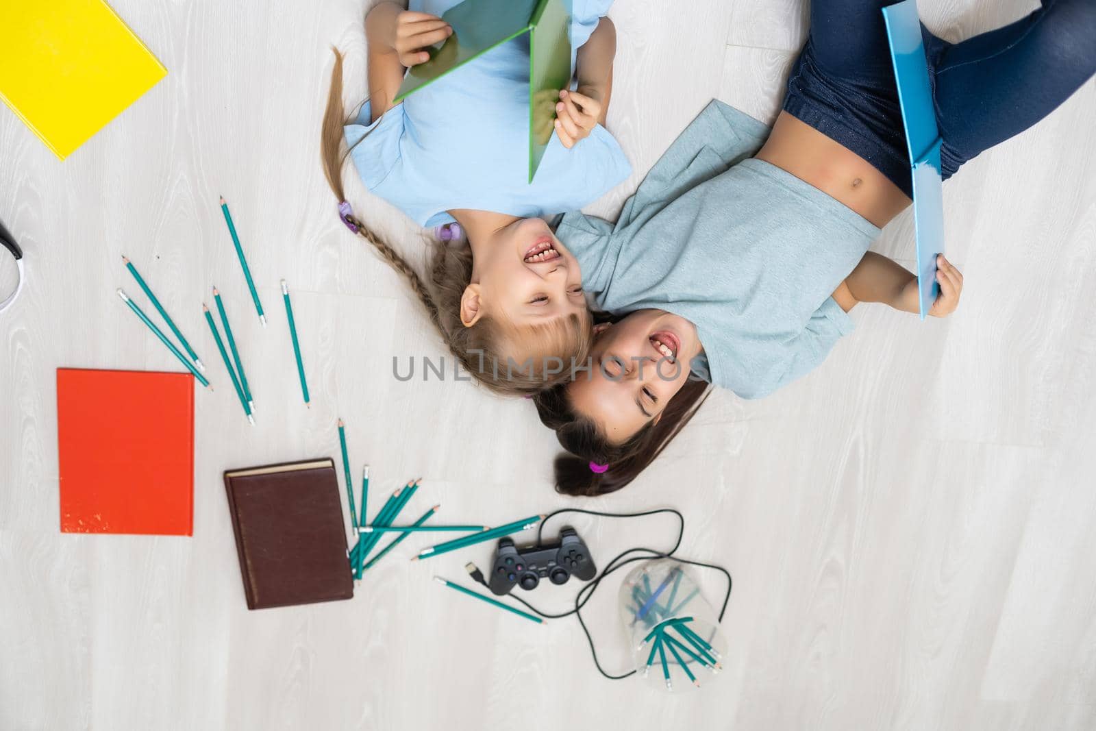 people, children, friends, literature and friendship concept - two happy girls lying on floor and reading book at home