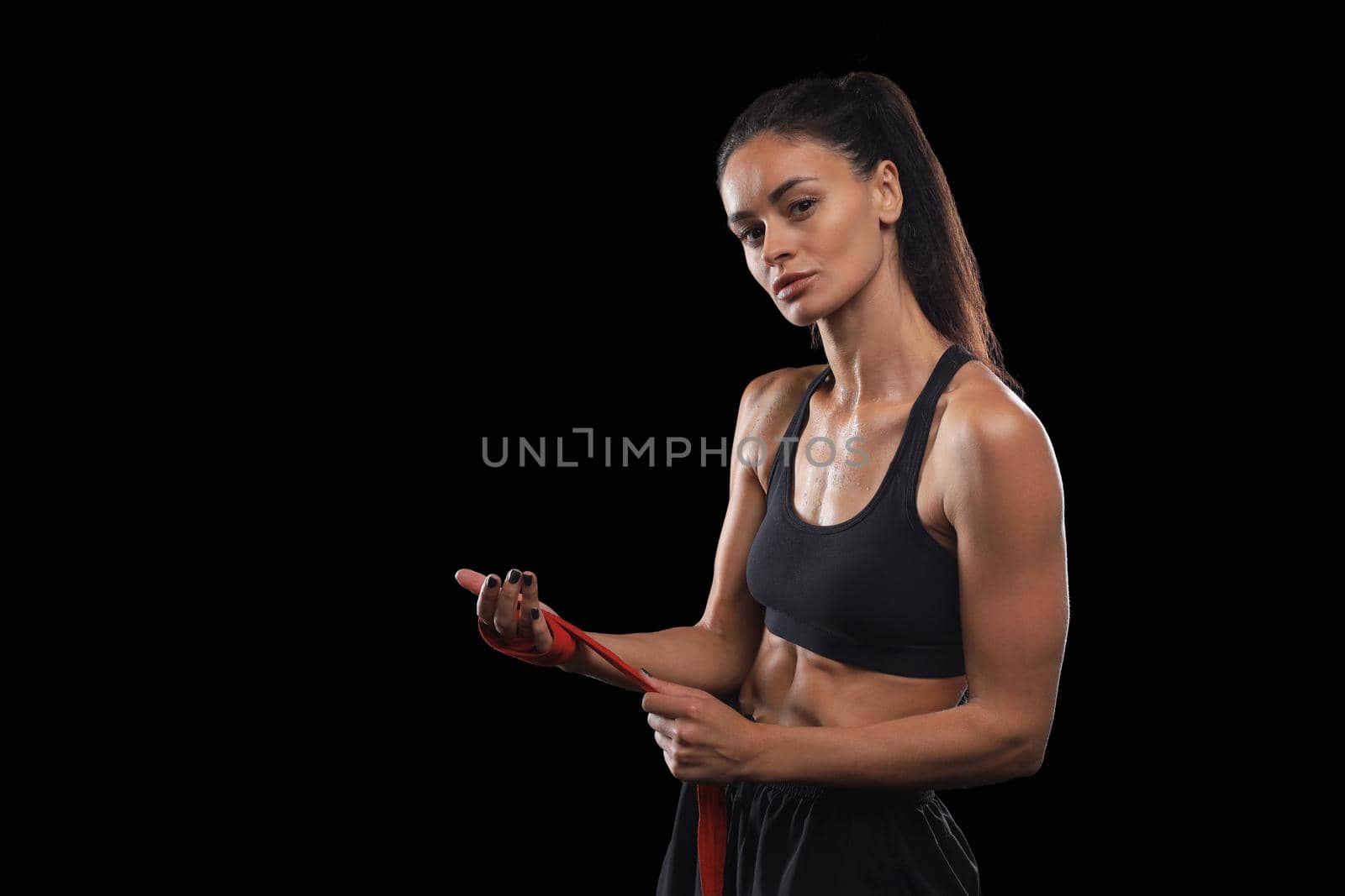 Beautiful and fit female fighter getting prepared for the fight or training, wrapping her hands with bandage tape against dark background