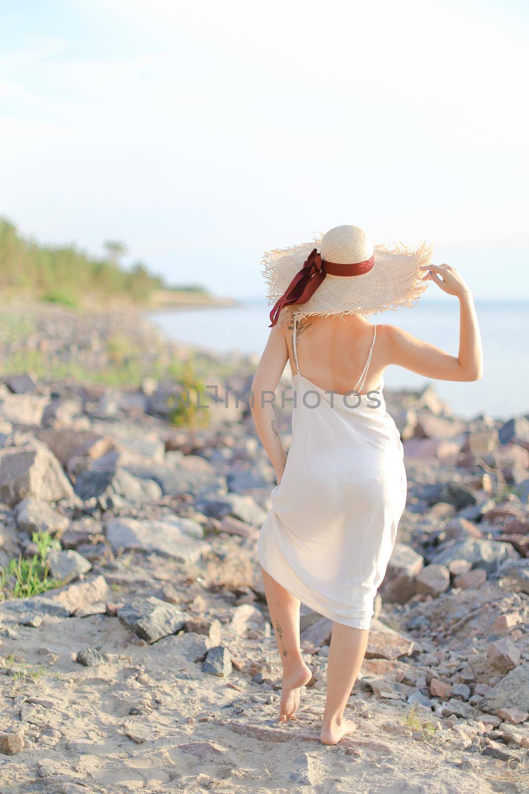 Back view of american woman in hat walking on shingle beach. by sisterspro