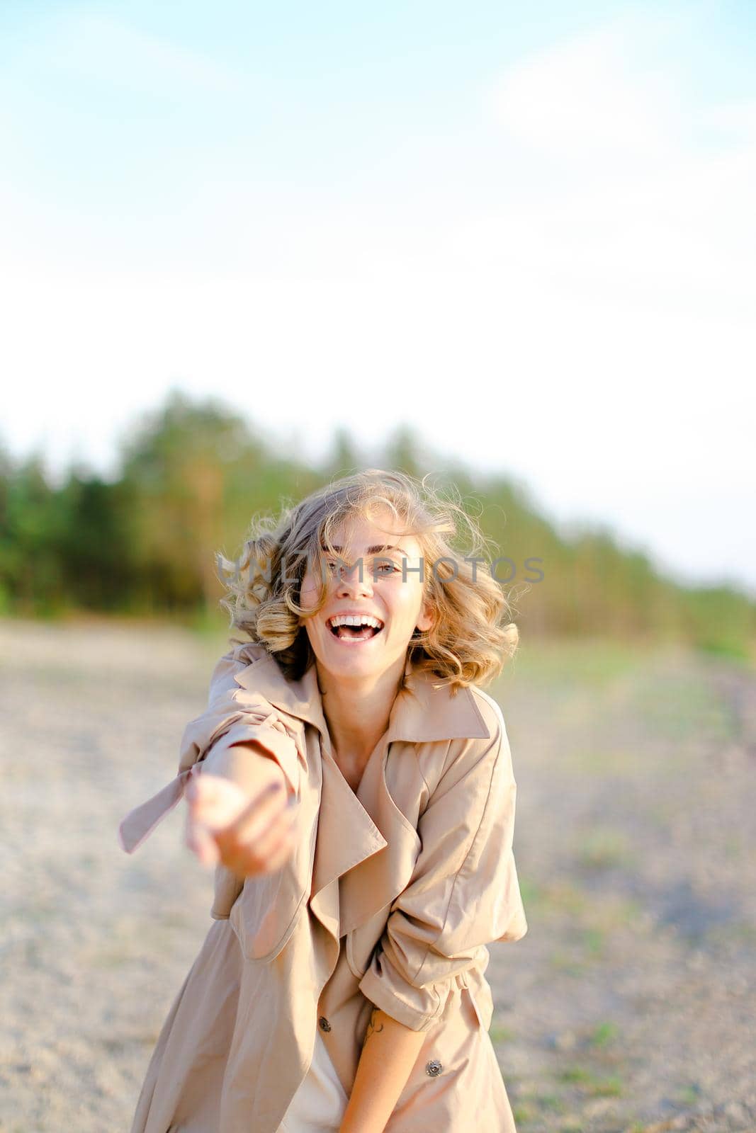 Young woman with outstretched hand on shingle beach wearing summer coat. by sisterspro