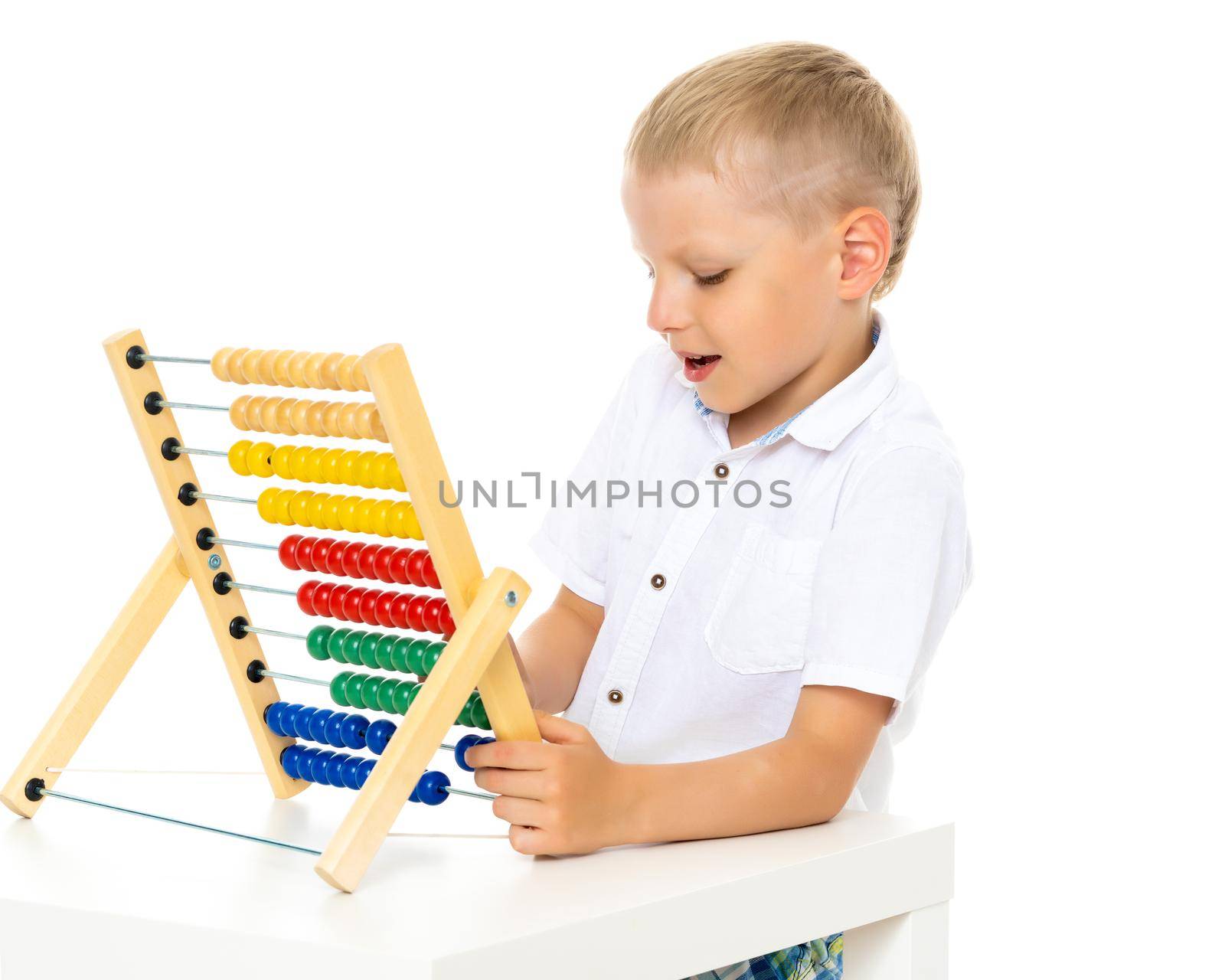 A cute little boy at school at a table studying mathematics. He uses abacus to solve mathematical problems. The concept of teaching a child in the family or at school.Isolated on white background.