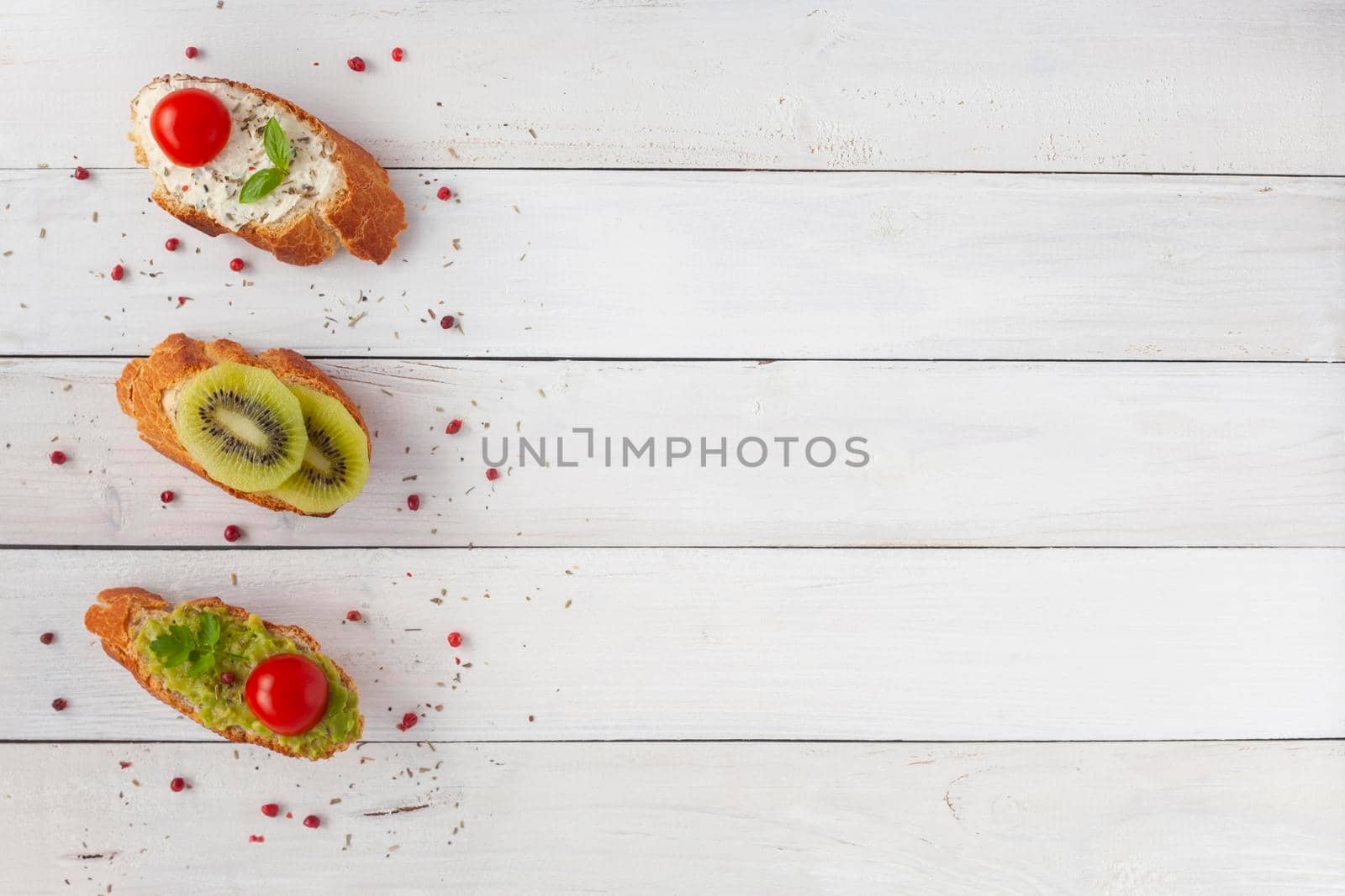 three homemade bright mini sandwichs with cream cheese and vegetables, on white wooden background, top view, copy space