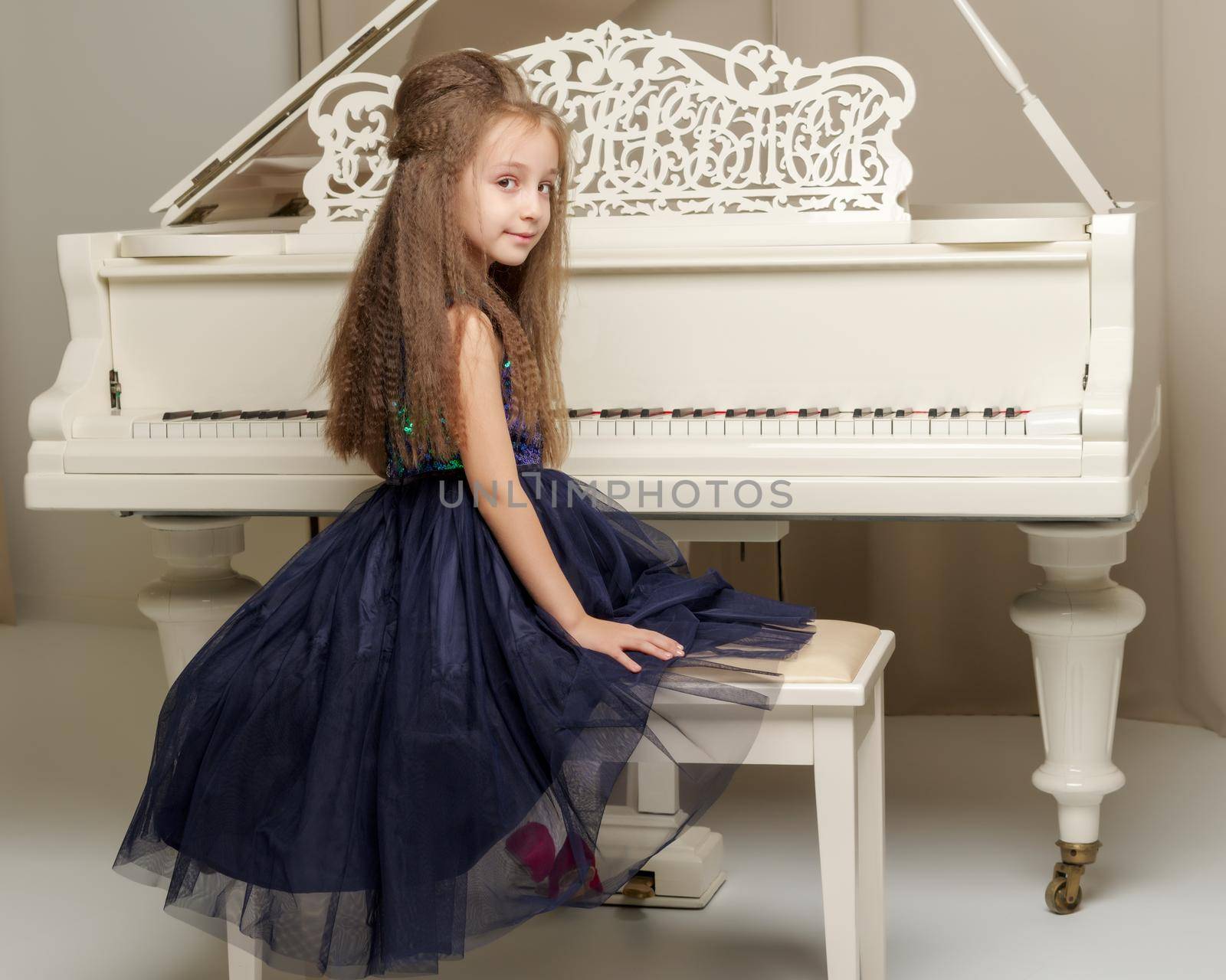 Beautiful little girl near a white grand piano. The concept of education and school, children's creativity.