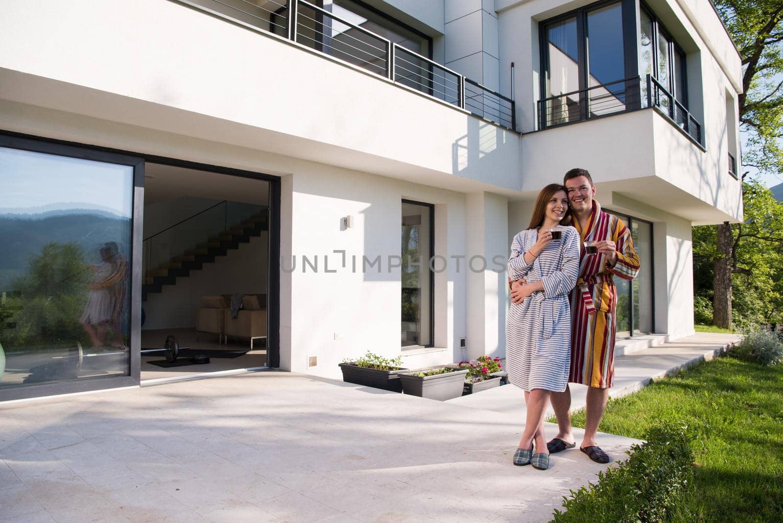 Young beautiful couple in bathrobes are enjoying morning coffee in front of their luxury home villa