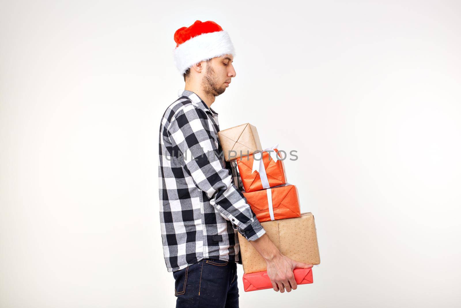 Holidays and presents concept - Funny man in Christmas hat holding many gift boxes on white background.