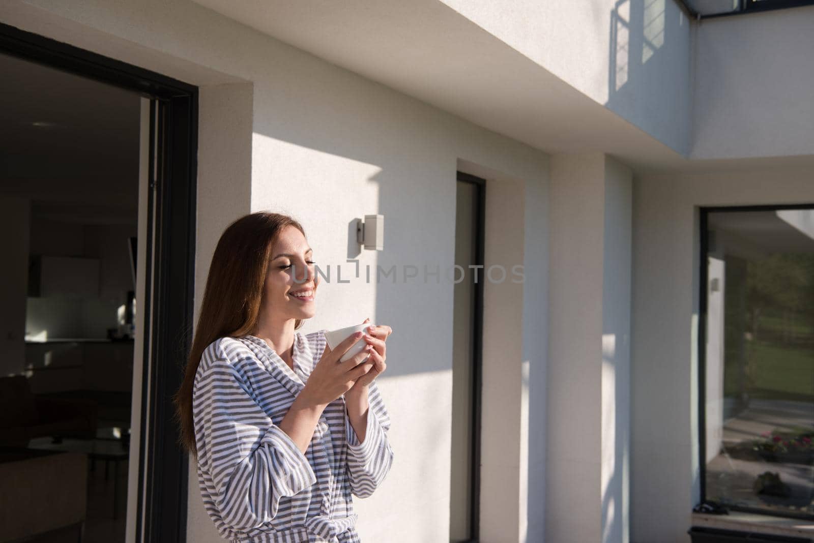 woman in a bathrobe enjoying morning coffee by dotshock