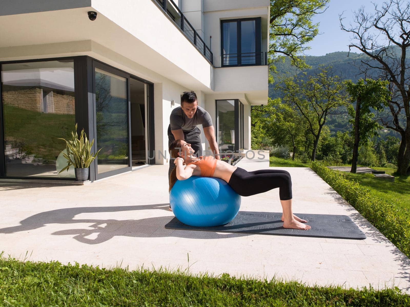 young beautiful woman and personal trainer doing exercise with pilates ball in front of her luxury home