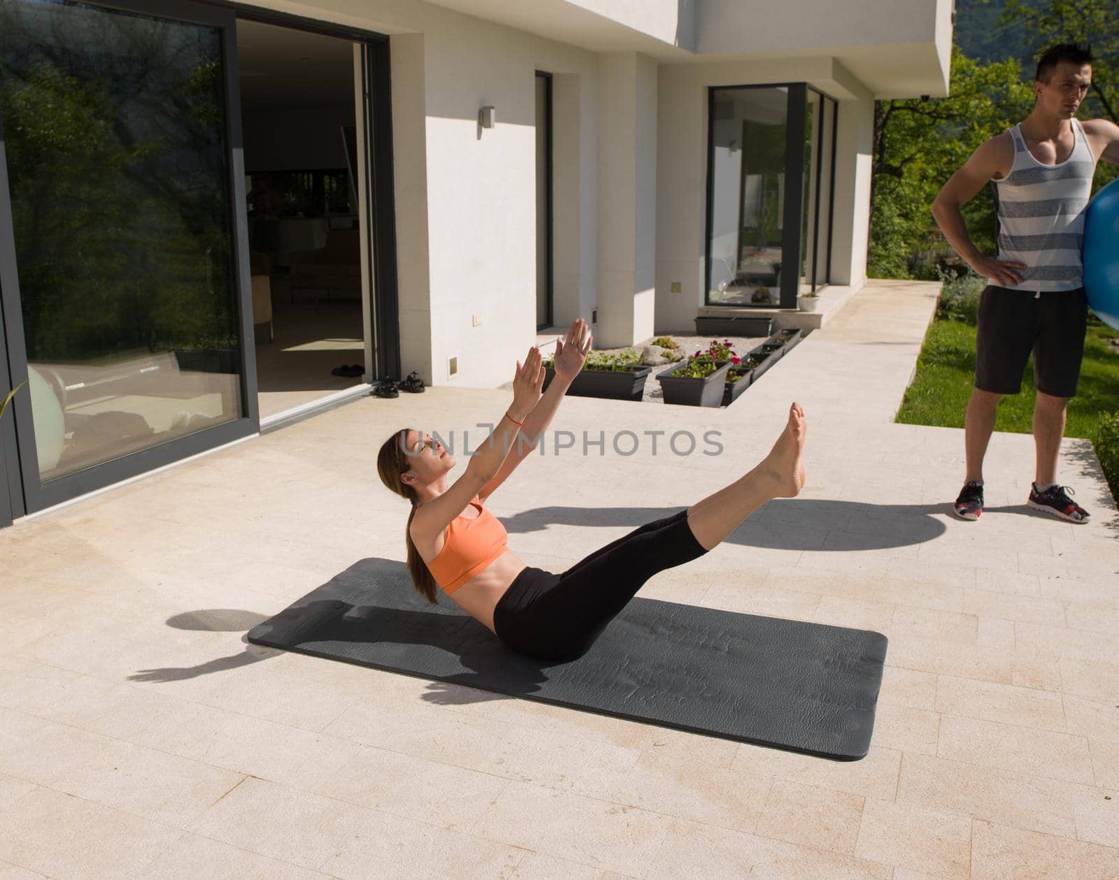 young beautiful woman and personal trainer doing exercise with pilates ball in front of her luxury home