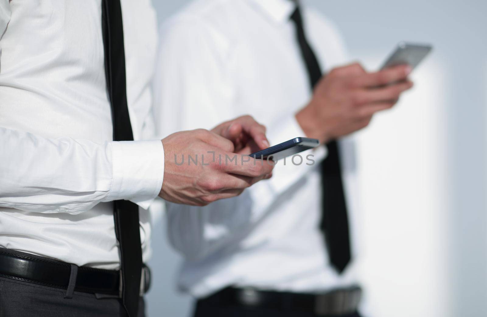 wo businessmen hold the phones in their hands in the office. a large plan.