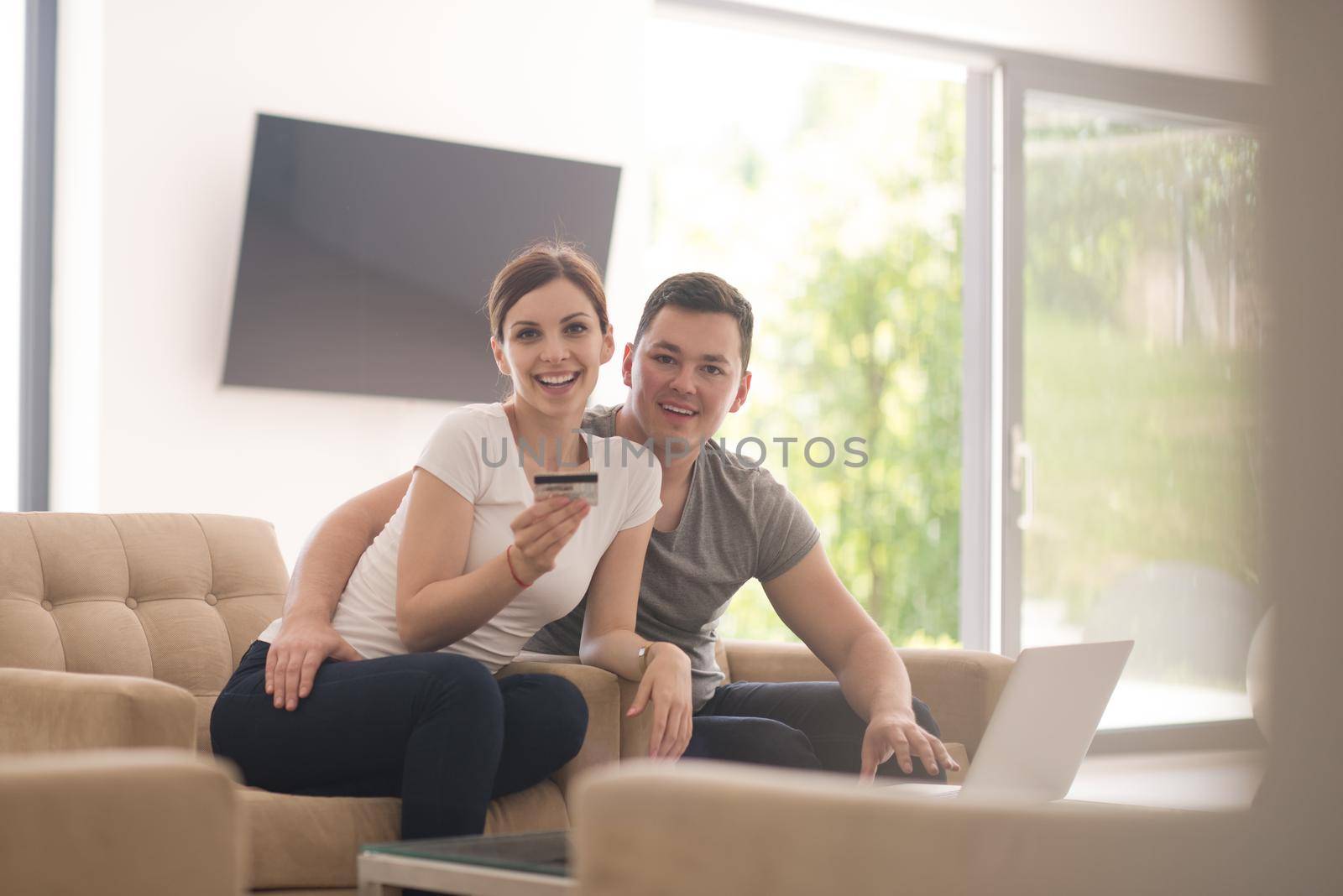 happy young couple buying online using laptop a computer and a credit card in their luxury home villa