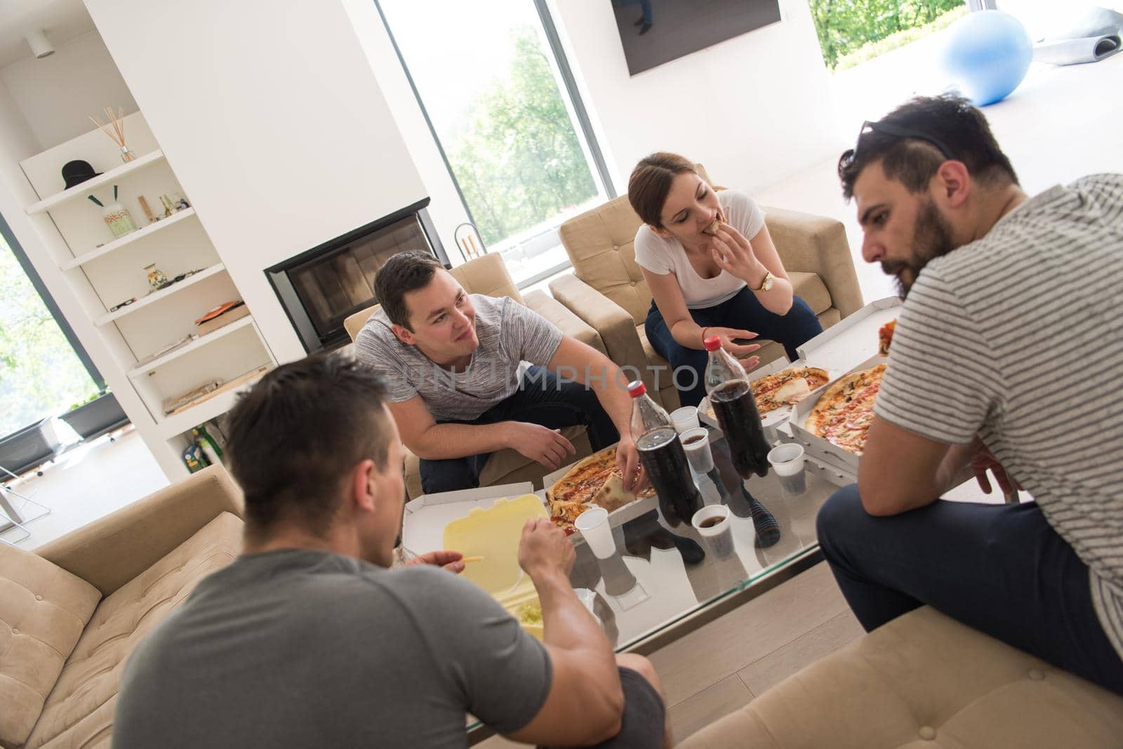 a group of young people cheerfully spending time while eating pizza in their luxury home villa