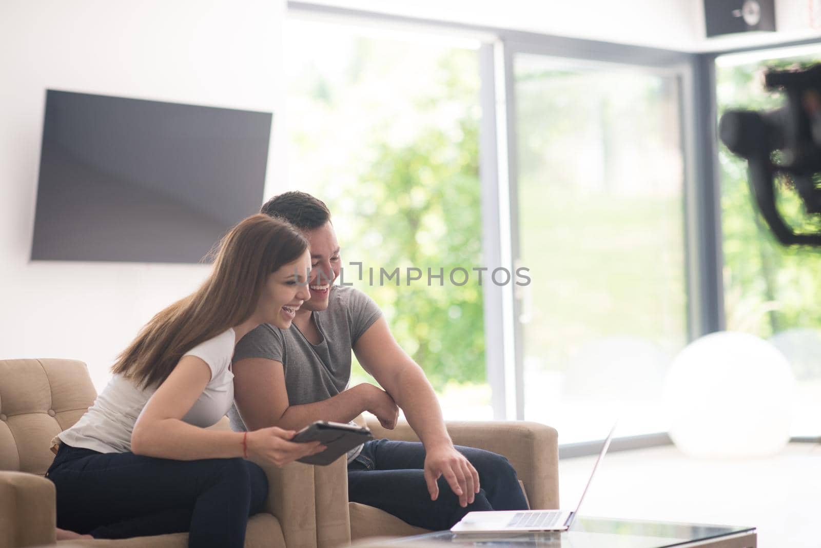 Young couple relaxing at luxurious home with tablet and laptop computers reading in the living room on the sofa couch.