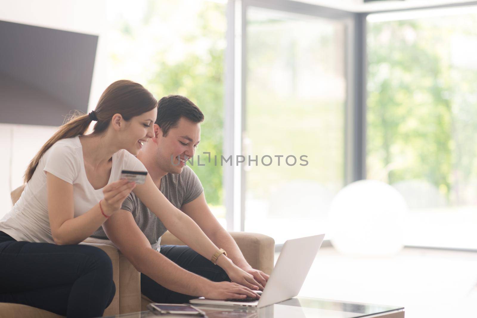 happy young couple buying online using laptop a computer and a credit card in their luxury home villa