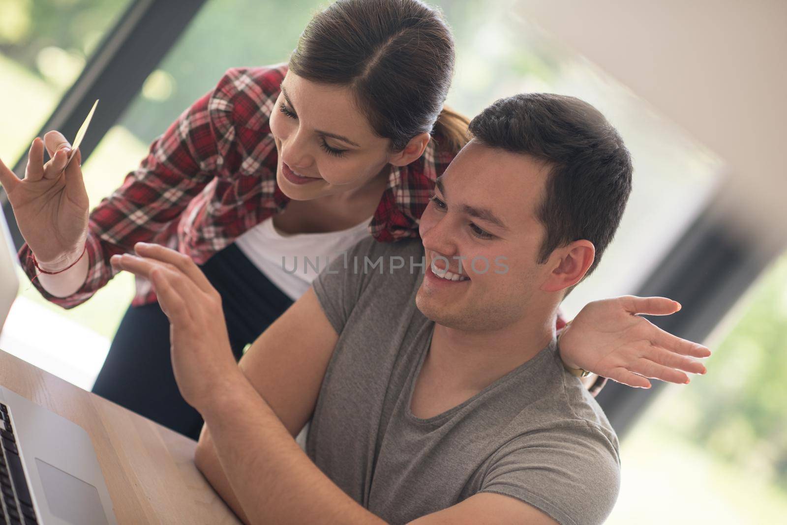 happy young couple buying online using laptop a computer and a credit card in their luxury home villa