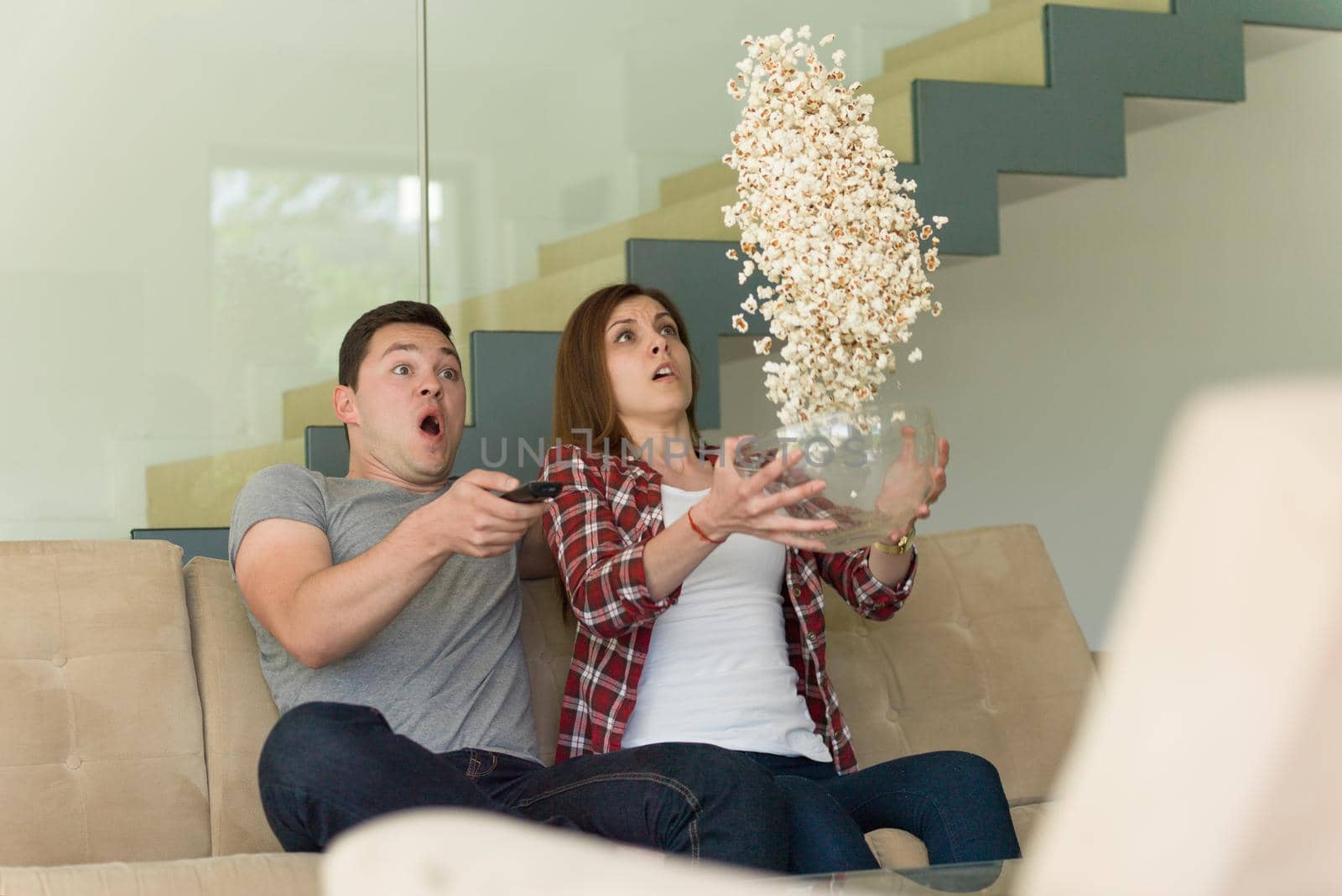 young handsome couple enjoying free time watching television with popcorn in their luxury home villa