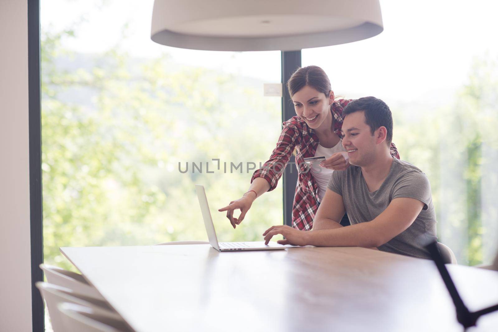 happy young couple buying online using laptop a computer and a credit card in their luxury home villa