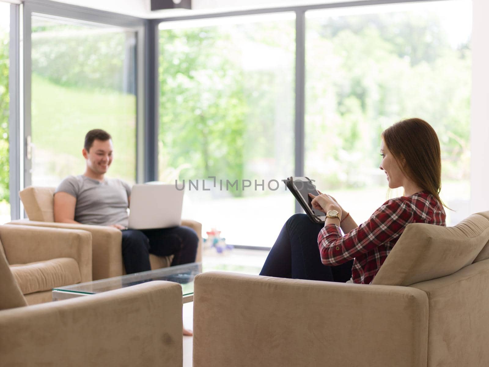 Young couple relaxing at luxurious home with tablet and laptop computers reading in the living room on the sofa couch.