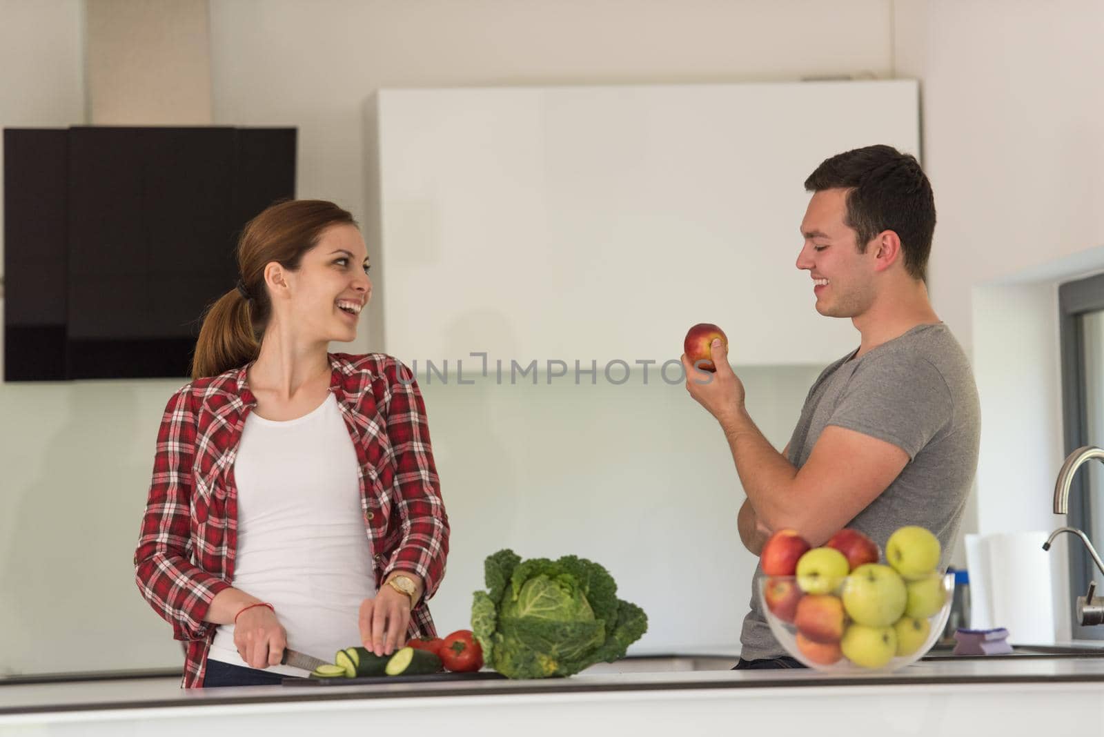 Young handsome couple in the kitchen  beautiful woman preparing a salad while the man eating an apple