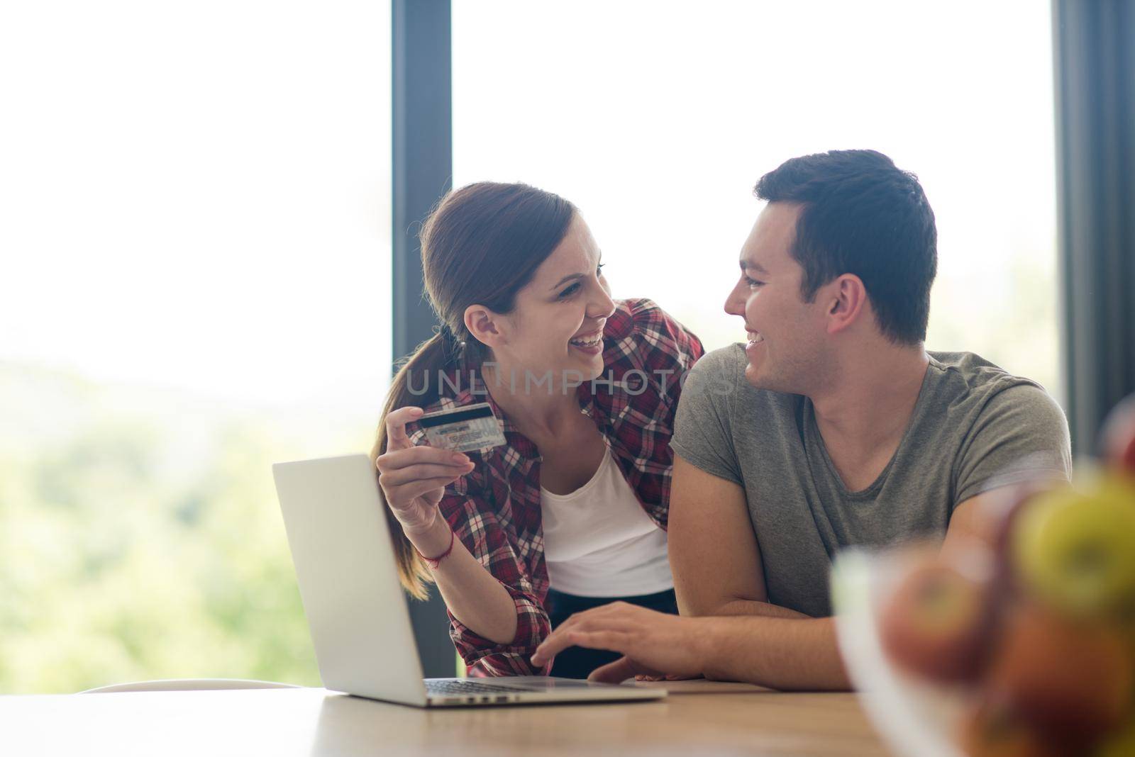 happy young couple buying online using laptop a computer and a credit card in their luxury home villa