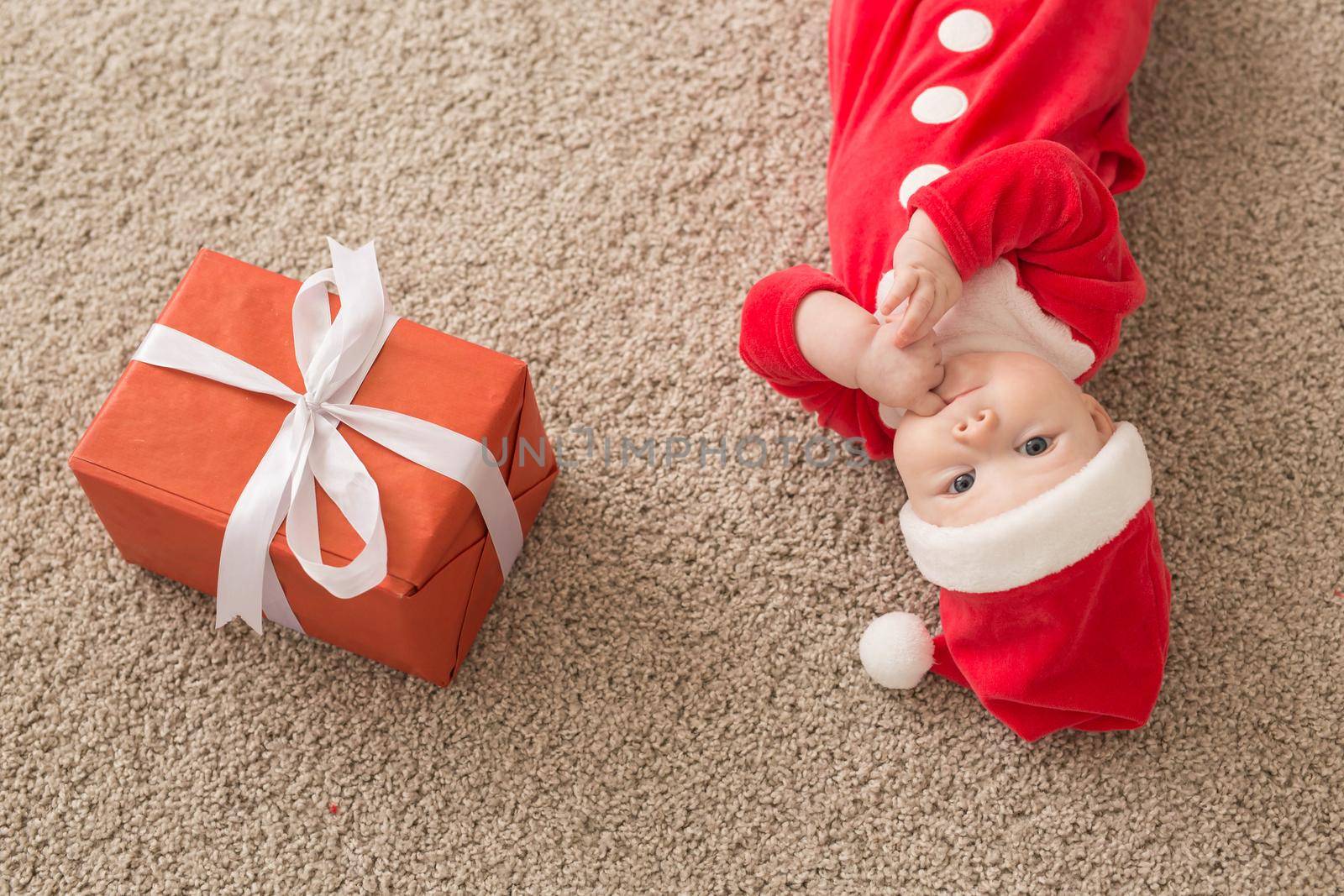 Beautiful little baby celebrates Christmas. New Year's holidays. Baby in a Christmas costume and in santa hat and gift box, top view.