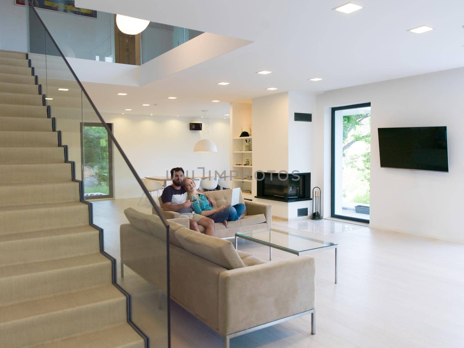 Young couple relaxes on the sofa in the luxury living room, using a laptop and remote control