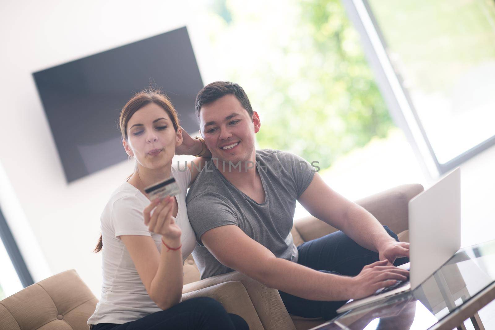 happy young couple buying online using laptop a computer and a credit card in their luxury home villa