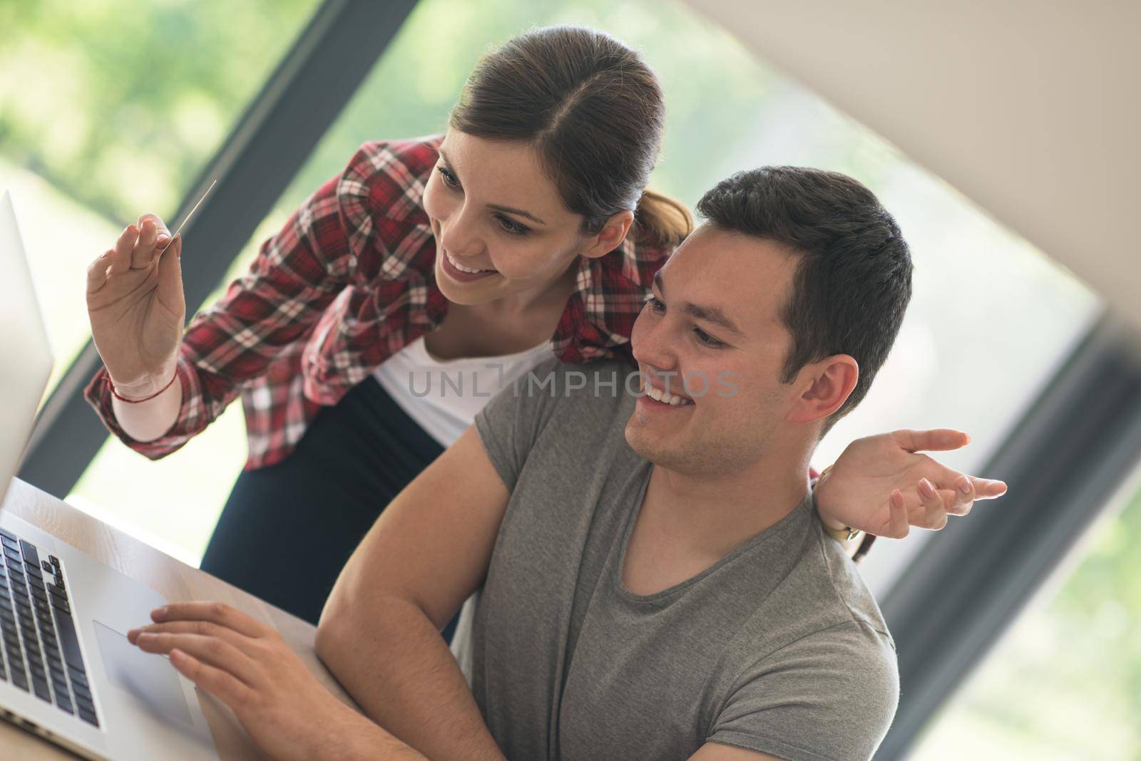 happy young couple buying online using laptop a computer and a credit card in their luxury home villa