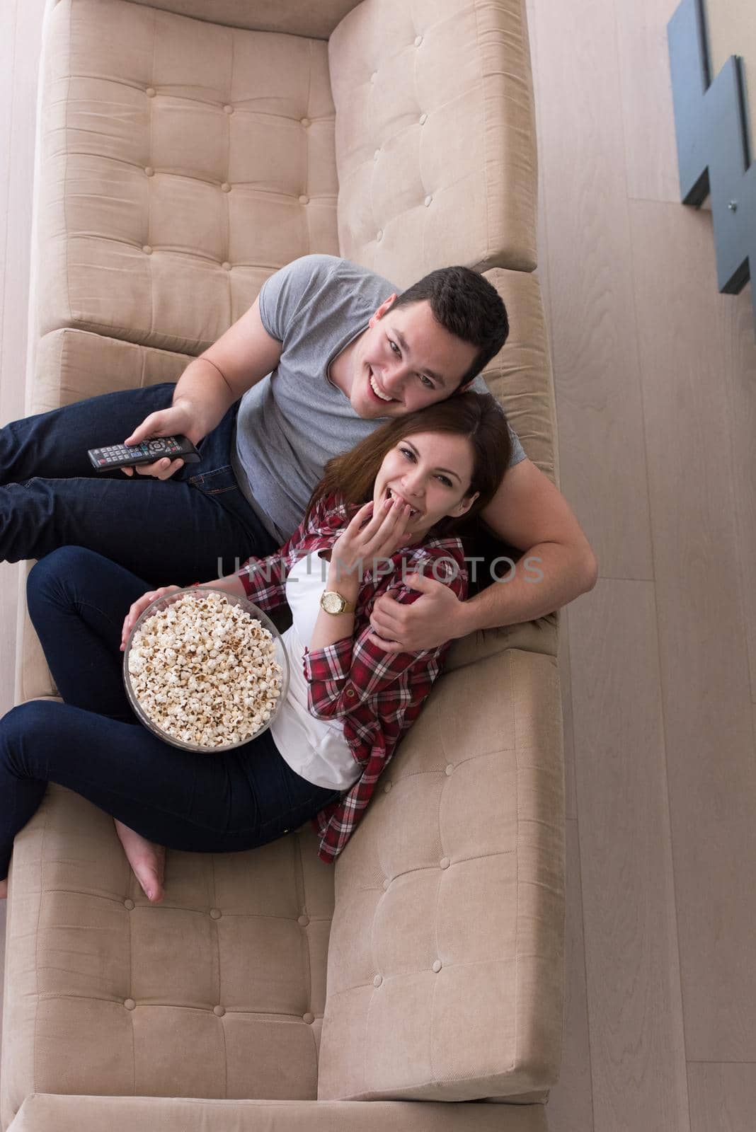 young handsome couple enjoying free time watching television with popcorn in their luxury home villa