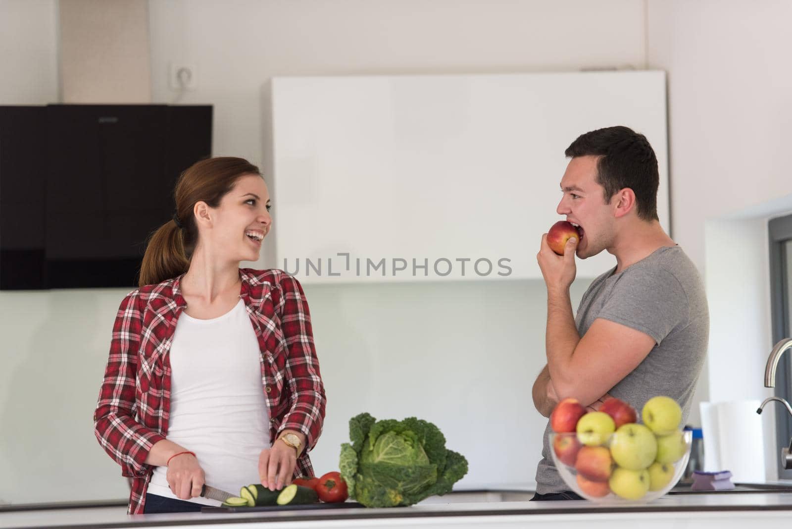 Young handsome couple in the kitchen  beautiful woman preparing a salad while the man eating an apple