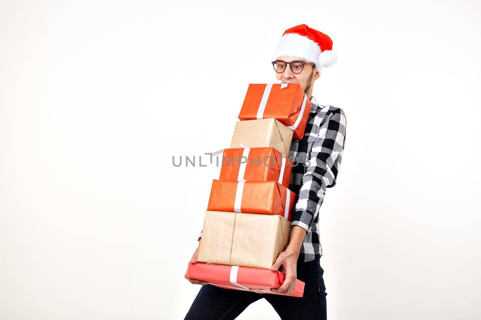 Holidays and presents concept - Funny man in Christmas hat holding many gift boxes on white background.