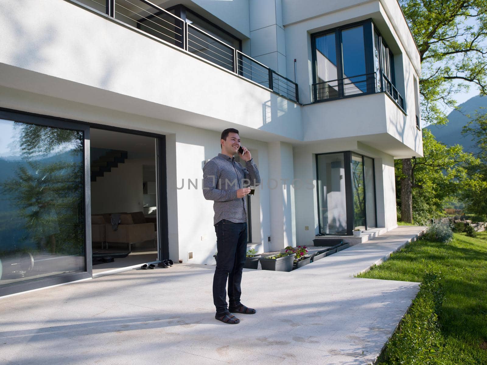 man using mobile phone in front of his luxury home villa by dotshock