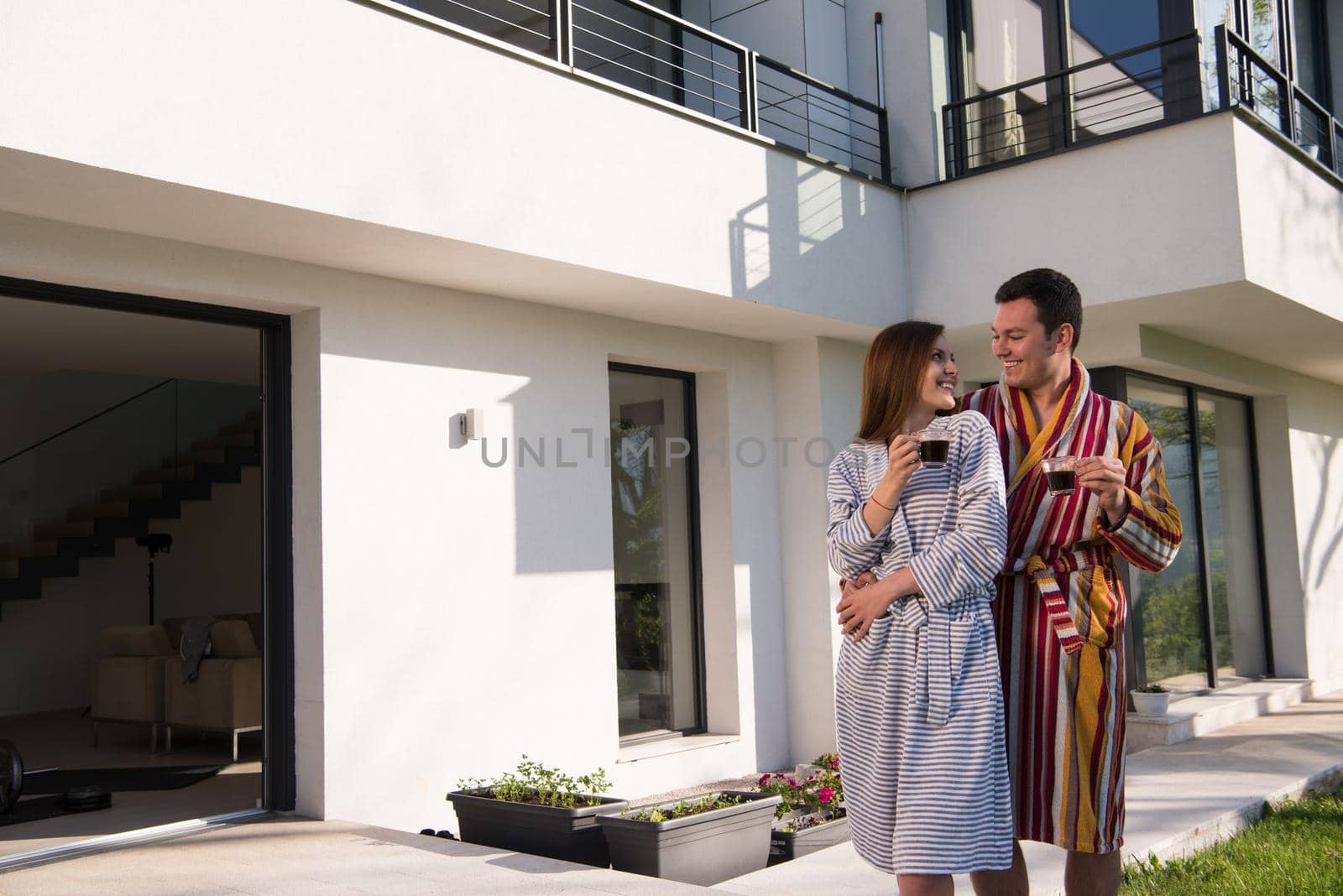 Young beautiful couple in bathrobes are enjoying morning coffee in front of their luxury home villa