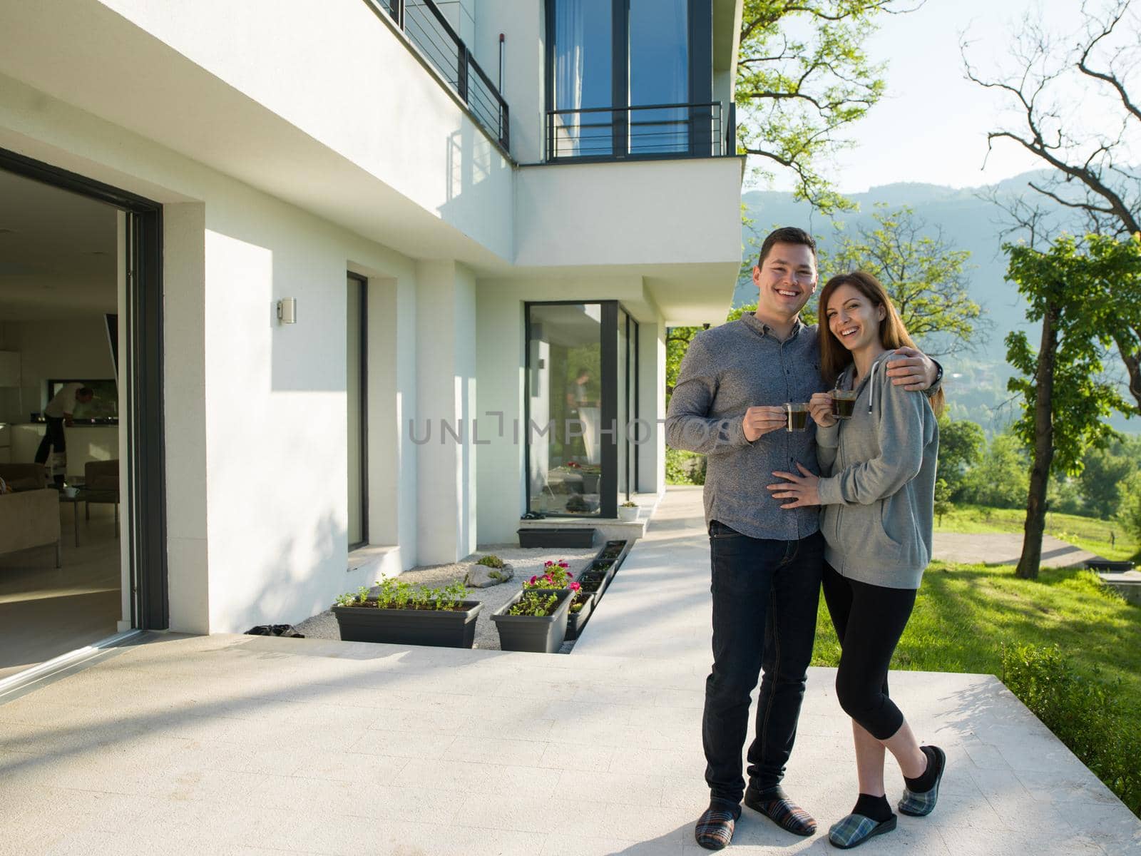 young beautiful handsome couple enjoying morning coffee in front of their luxury home villa