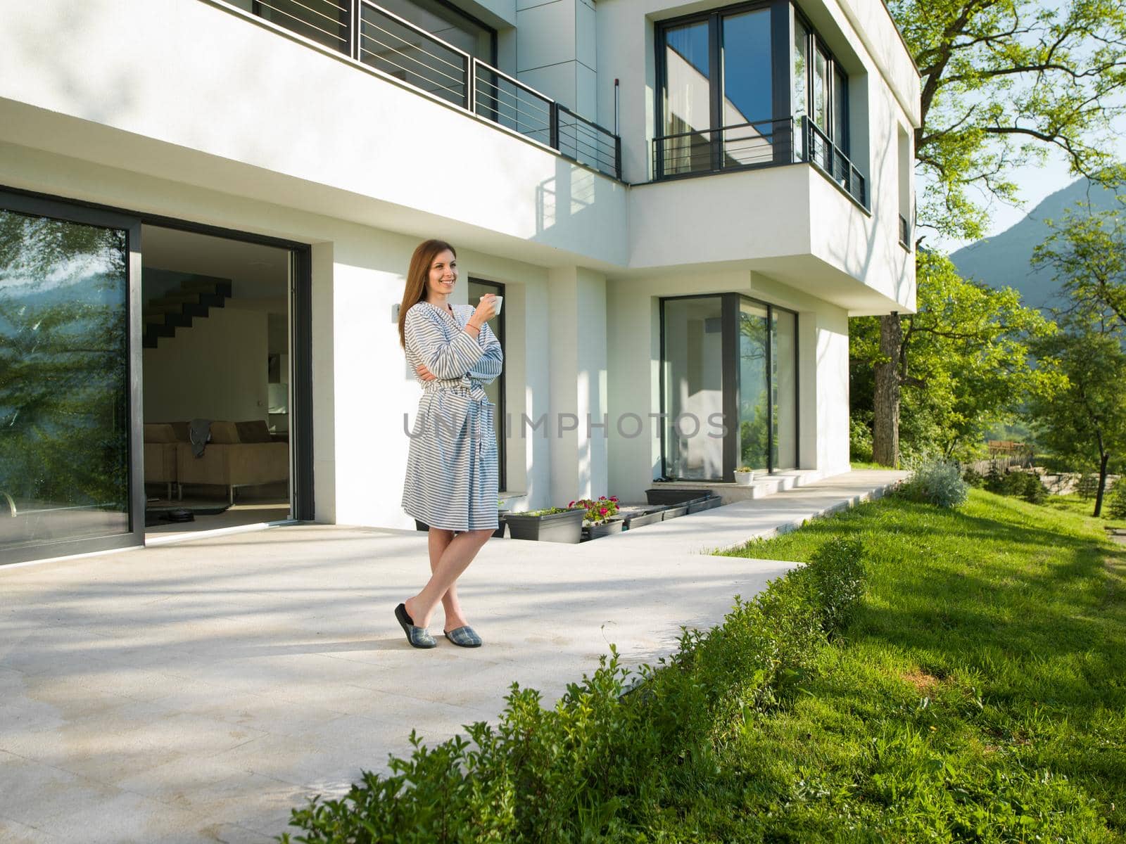 young beautiful woman in a bathrobe enjoying morning coffee in front of her luxury home villa