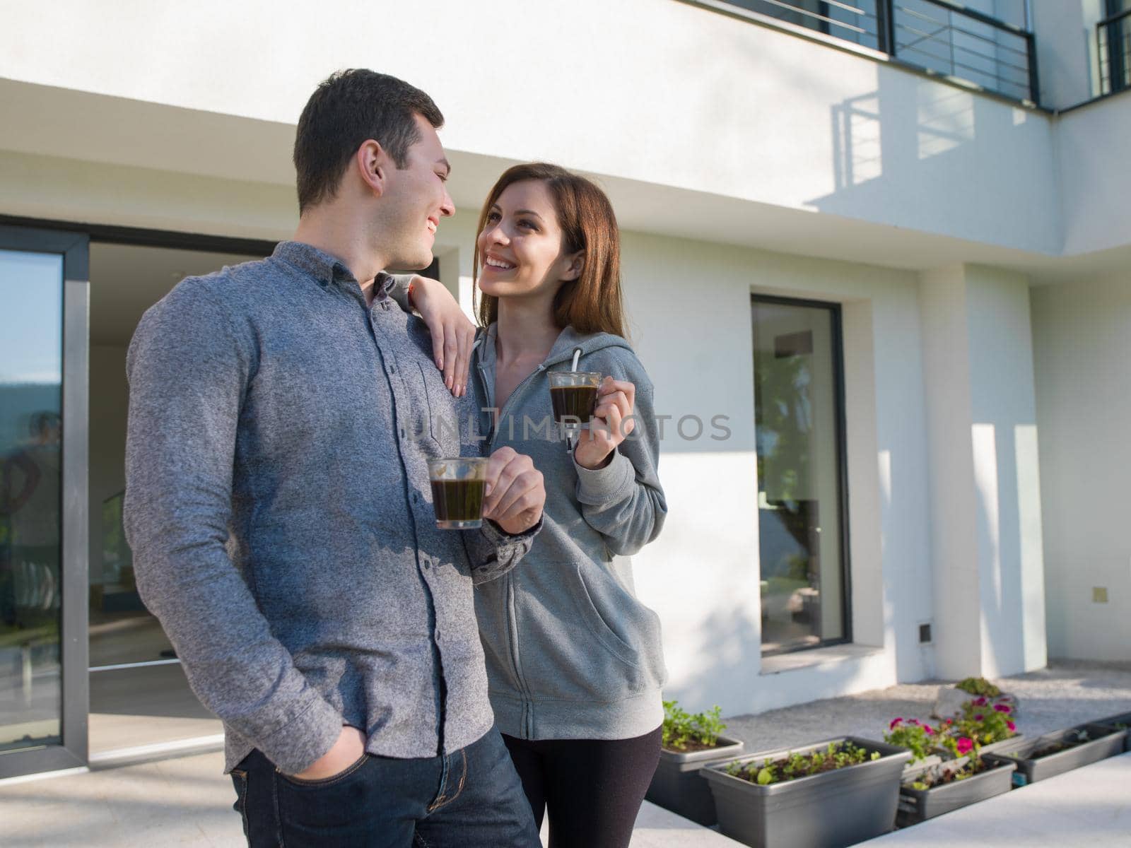 young beautiful handsome couple enjoying morning coffee in front of their luxury home villa