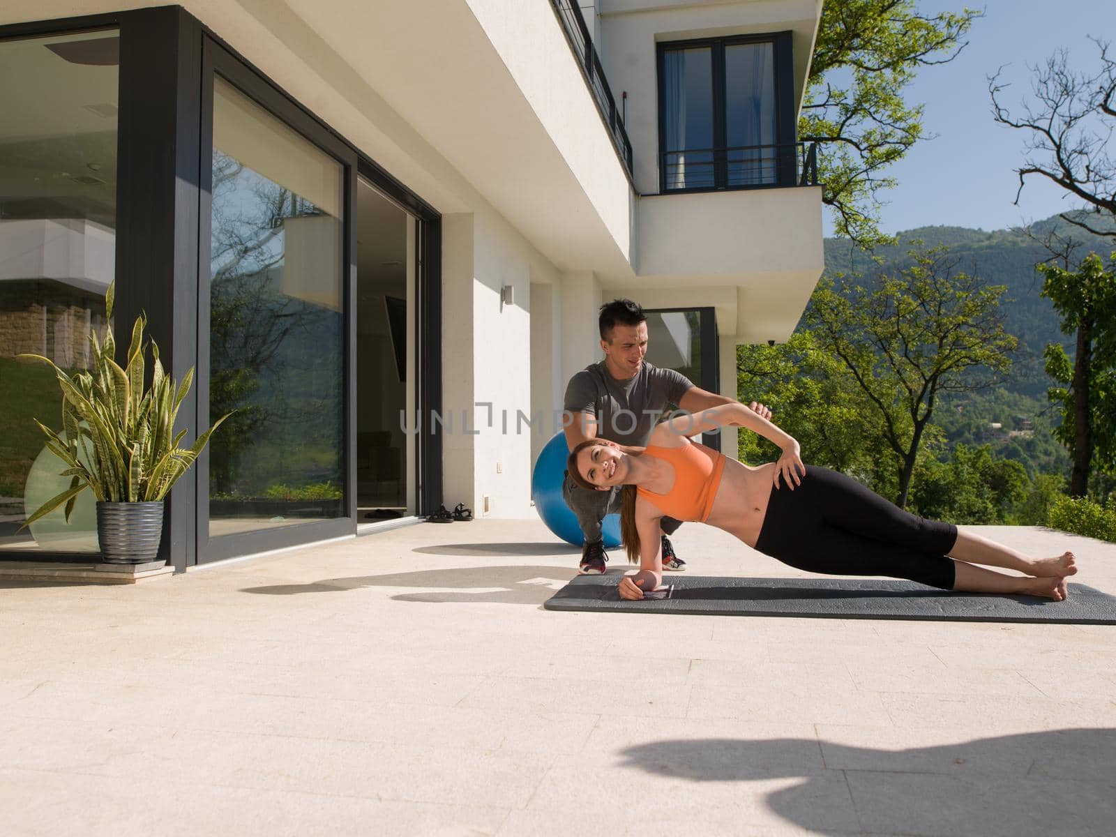 young handsome woman with personal trainer doing morning yoga exercises in front of her luxury home villa