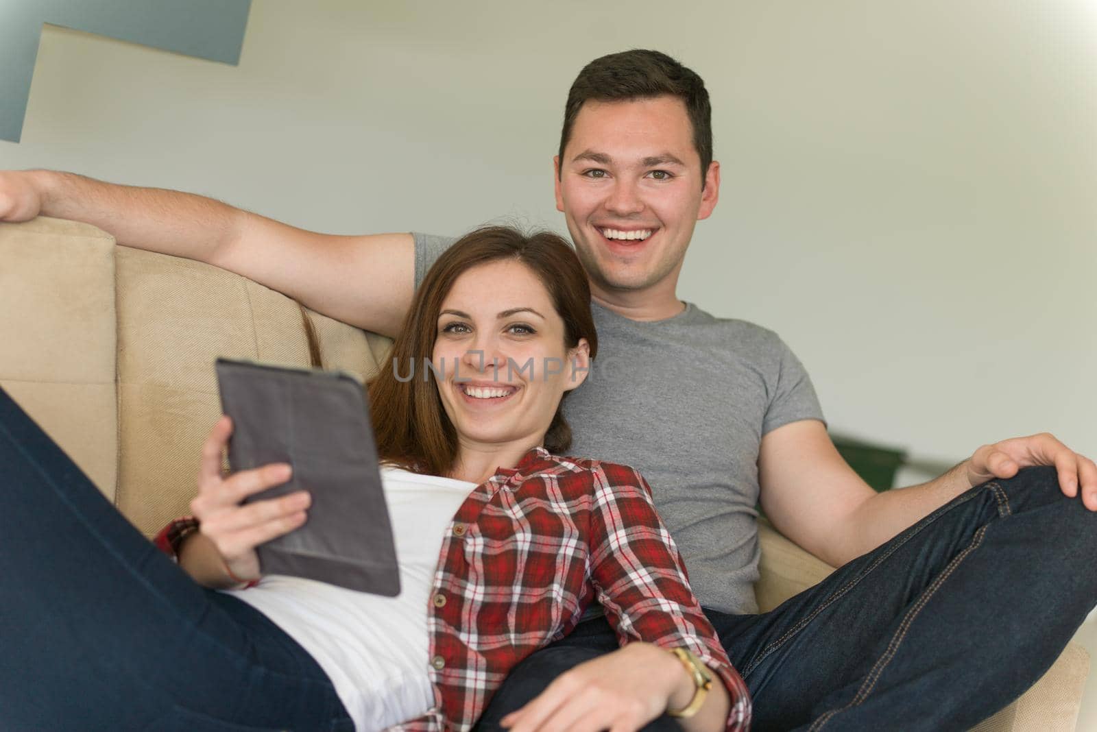 Young couple relaxing at luxurious home with tablet computers reading in the living room on the sofa couch.