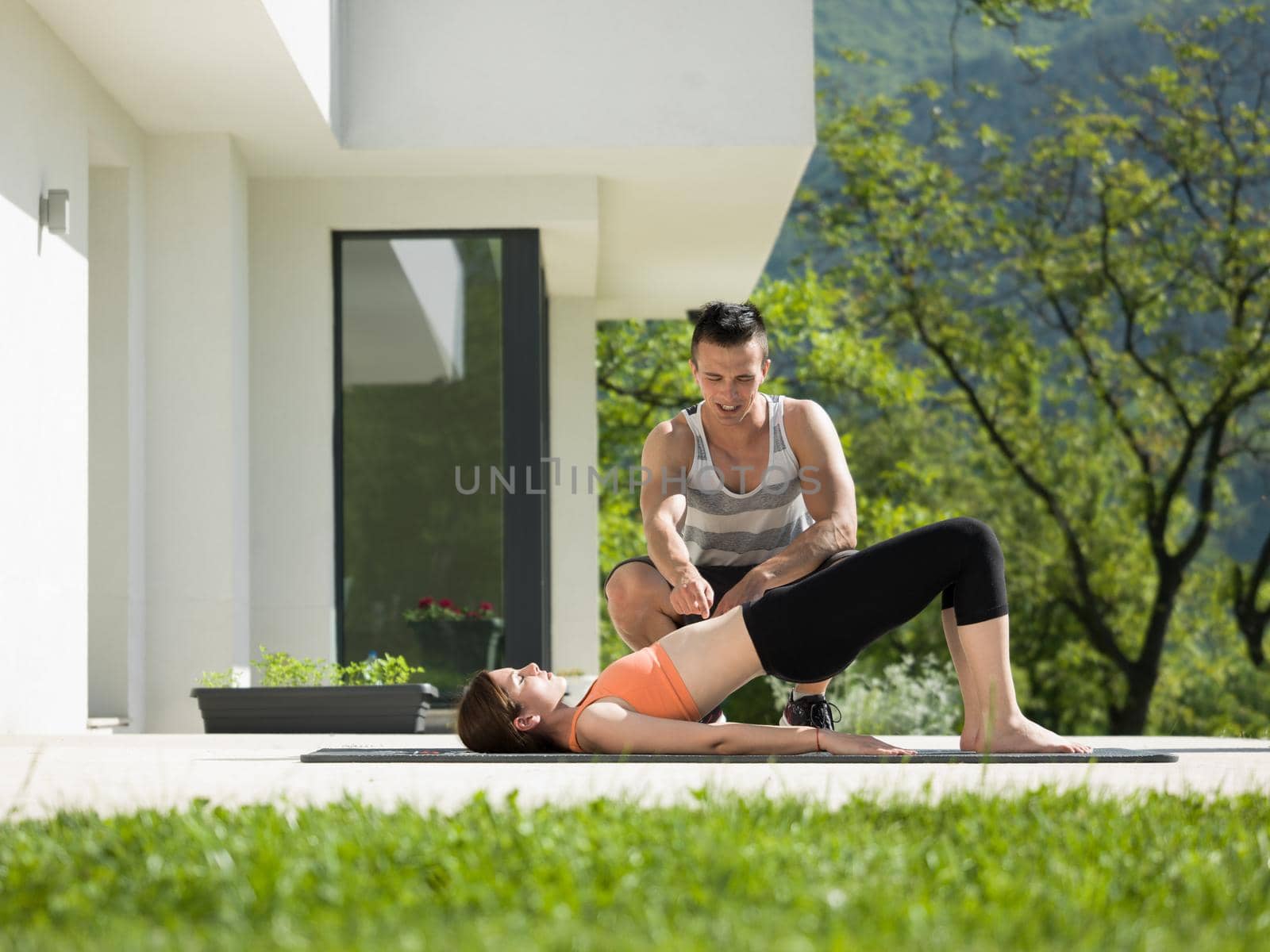 young handsome woman with personal trainer doing morning yoga exercises in front of her luxury home villa