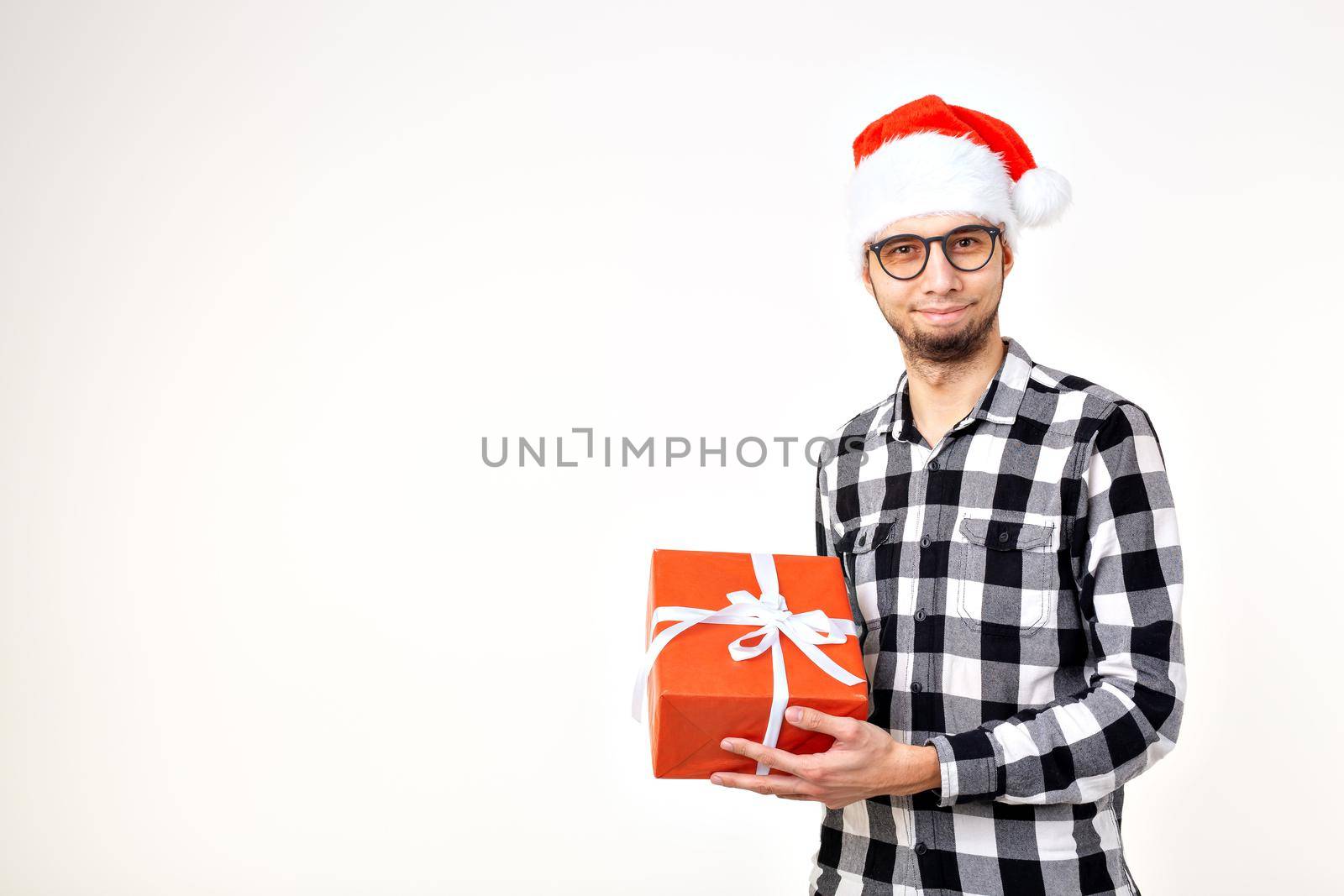 Holidays and presents concept - Funny man in Christmas hat holding gift box on white background with copy space by Satura86