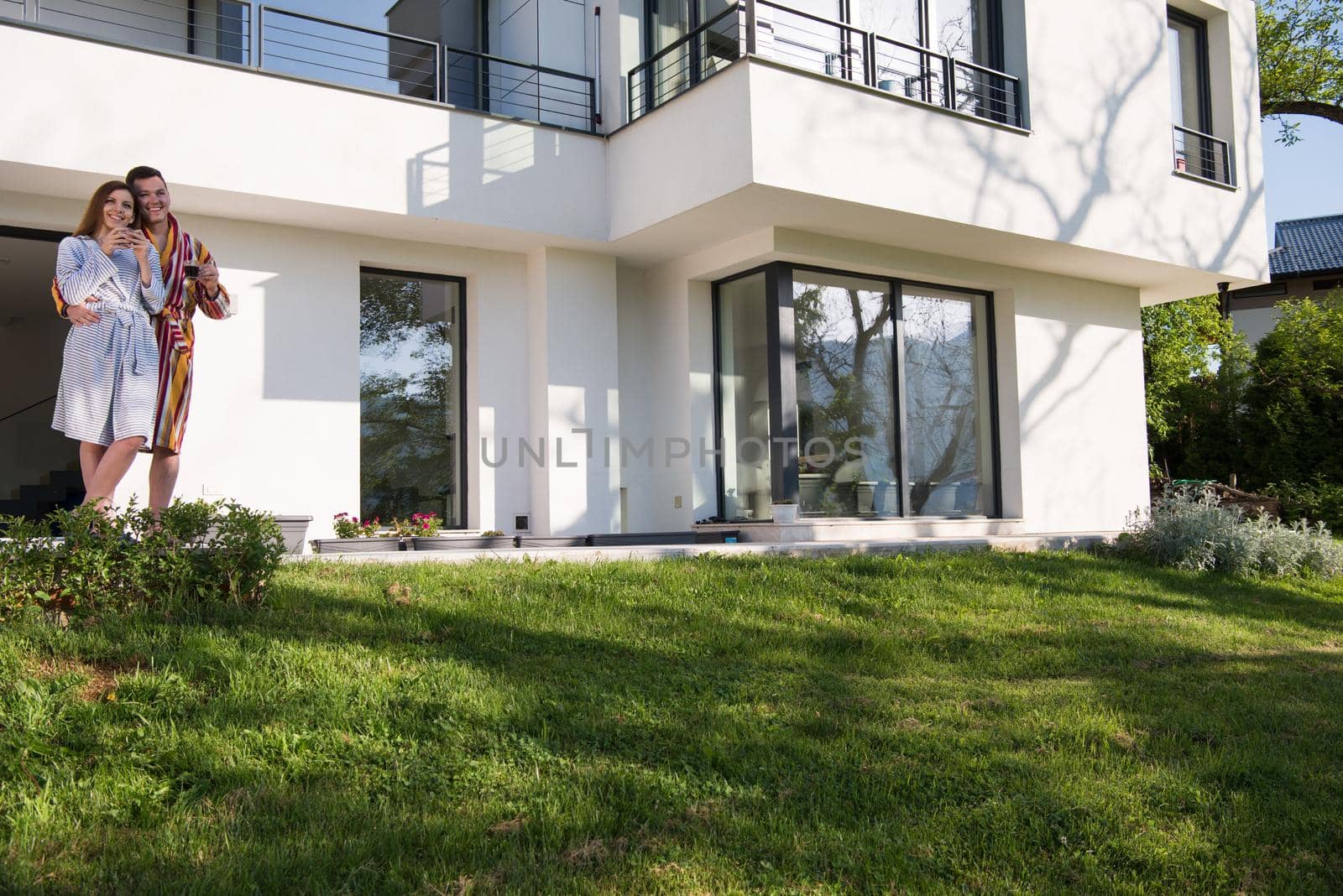 Young beautiful couple in bathrobes are enjoying morning coffee in front of their luxury home villa